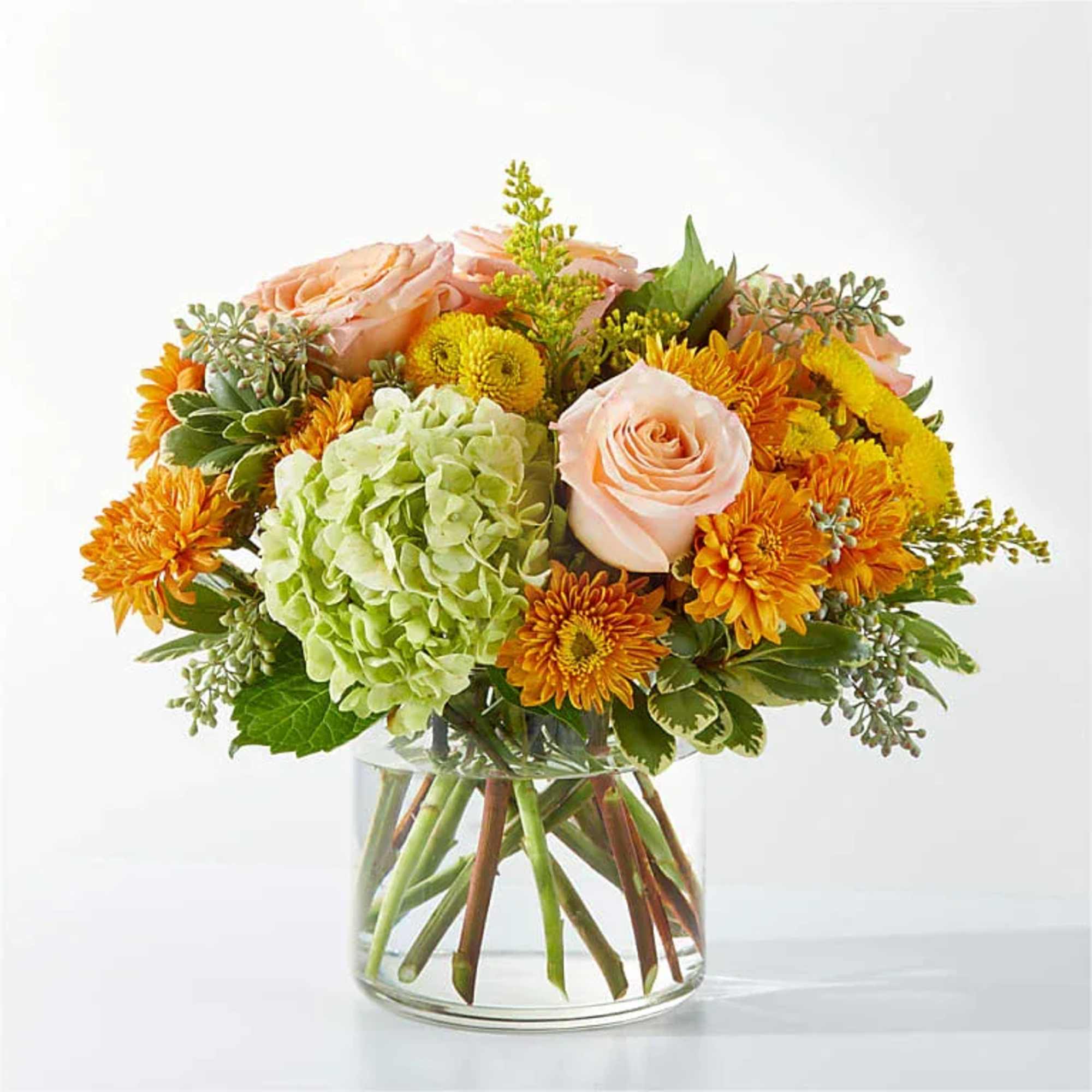 Peach roses and orange mums in a clear glass vase with a green hydrangea bloom