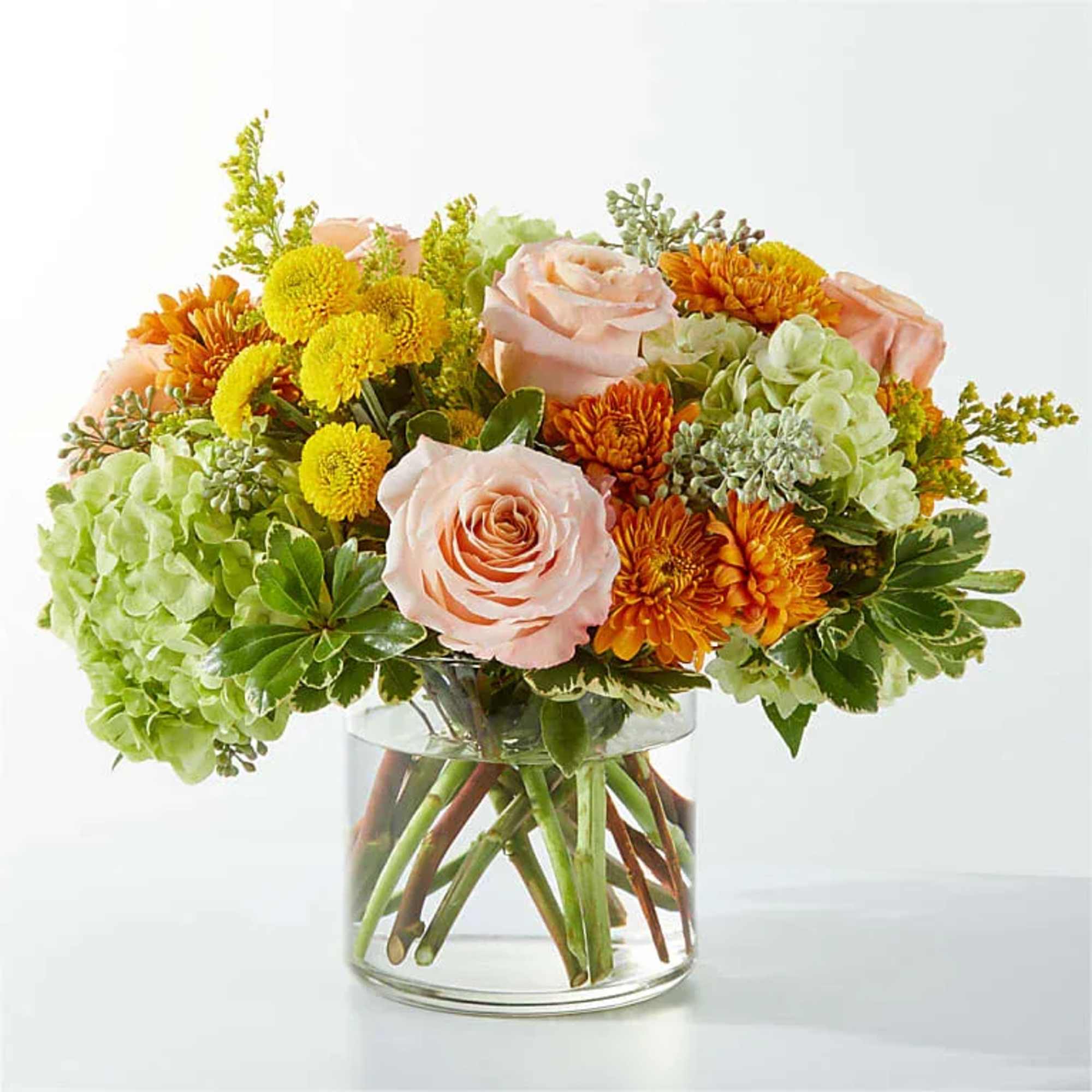 Bouquet of peach roses, green hydrangeas, and orange mums in a glass vase