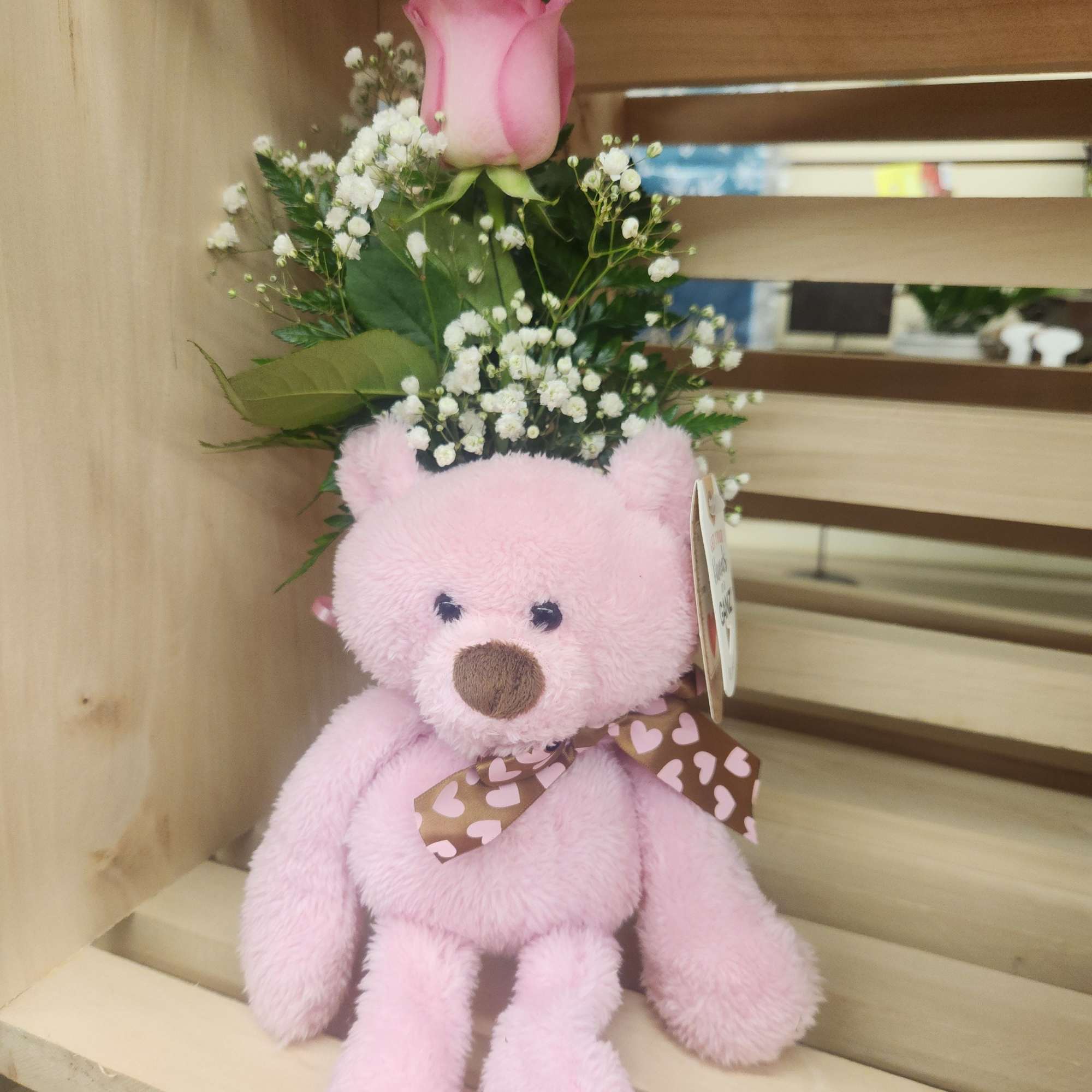 Pink teddy bear with a small pink rose and baby's breath arrangement