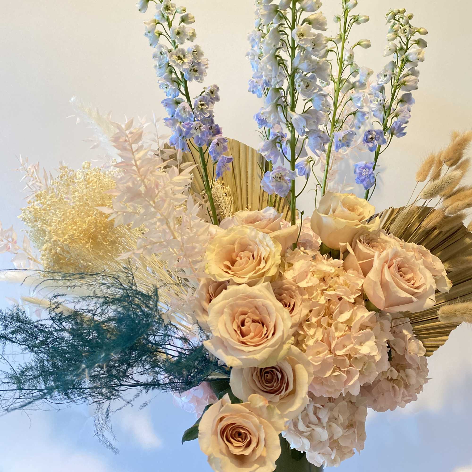 Peach roses and blue delphinium in a tall vase