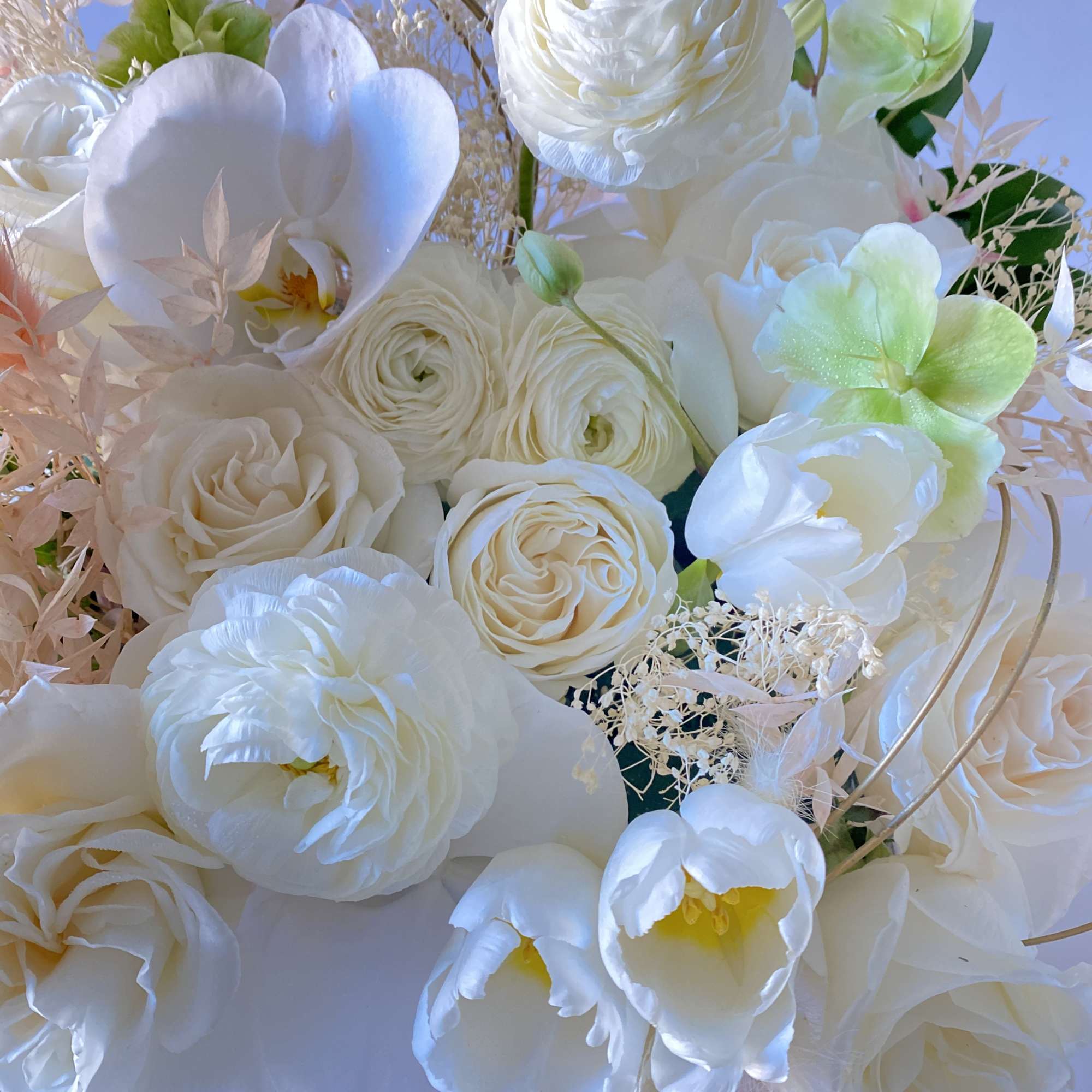 White bouquet with roses, ranunculus, and orchids against a blue background