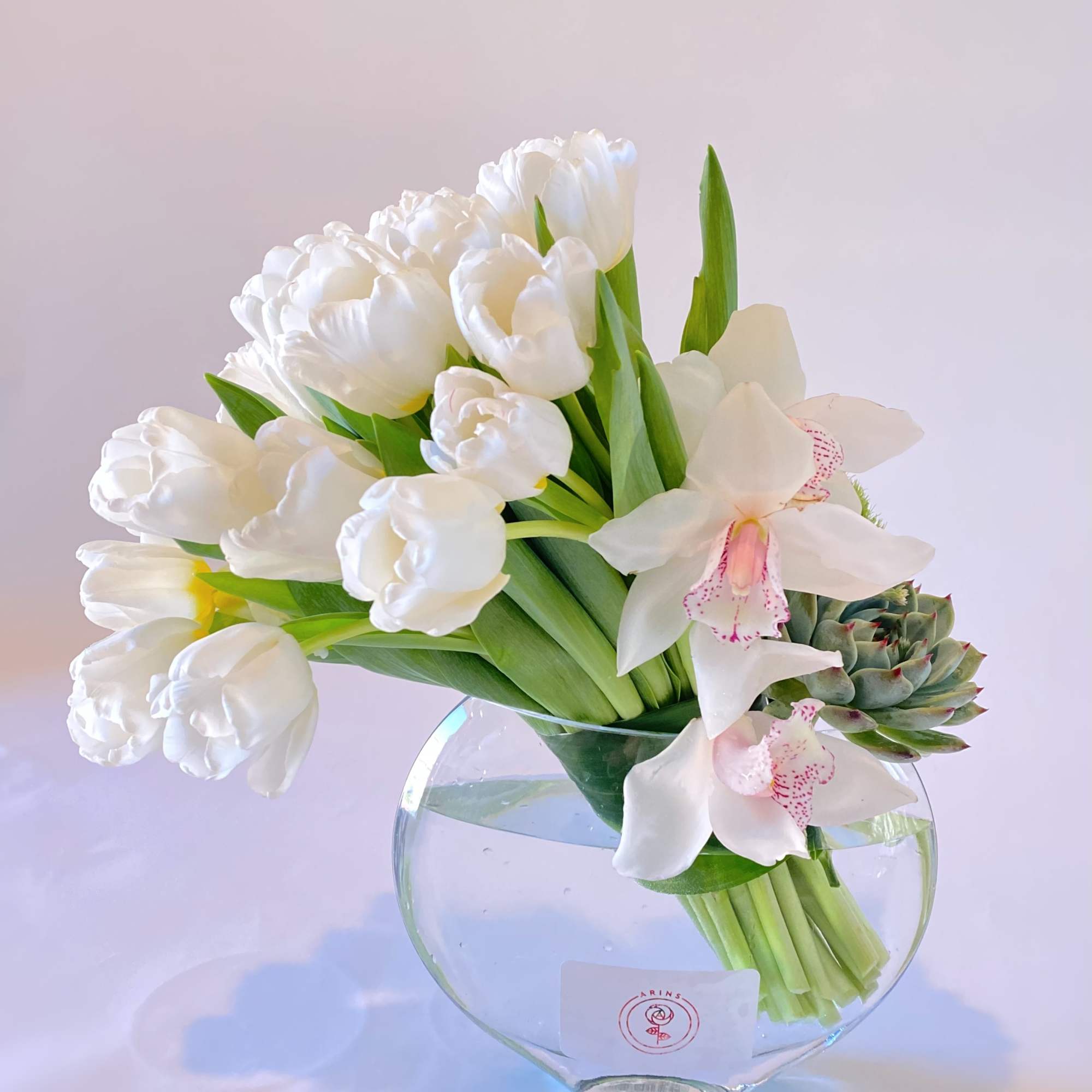 White tulips and orchids arranged in a clear glass vase with a succulent accent