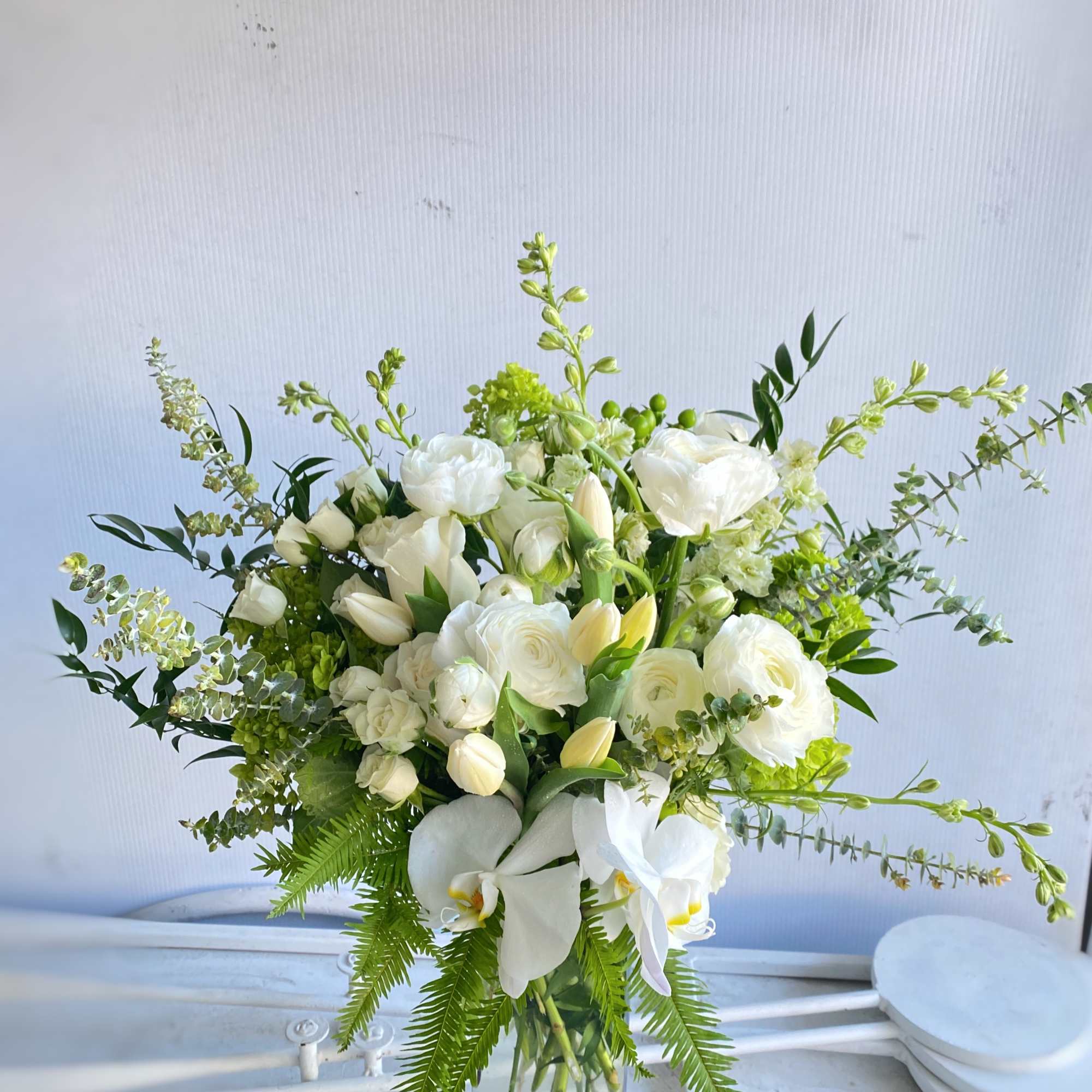 White floral arrangement in a clear glass vase with orchids and roses