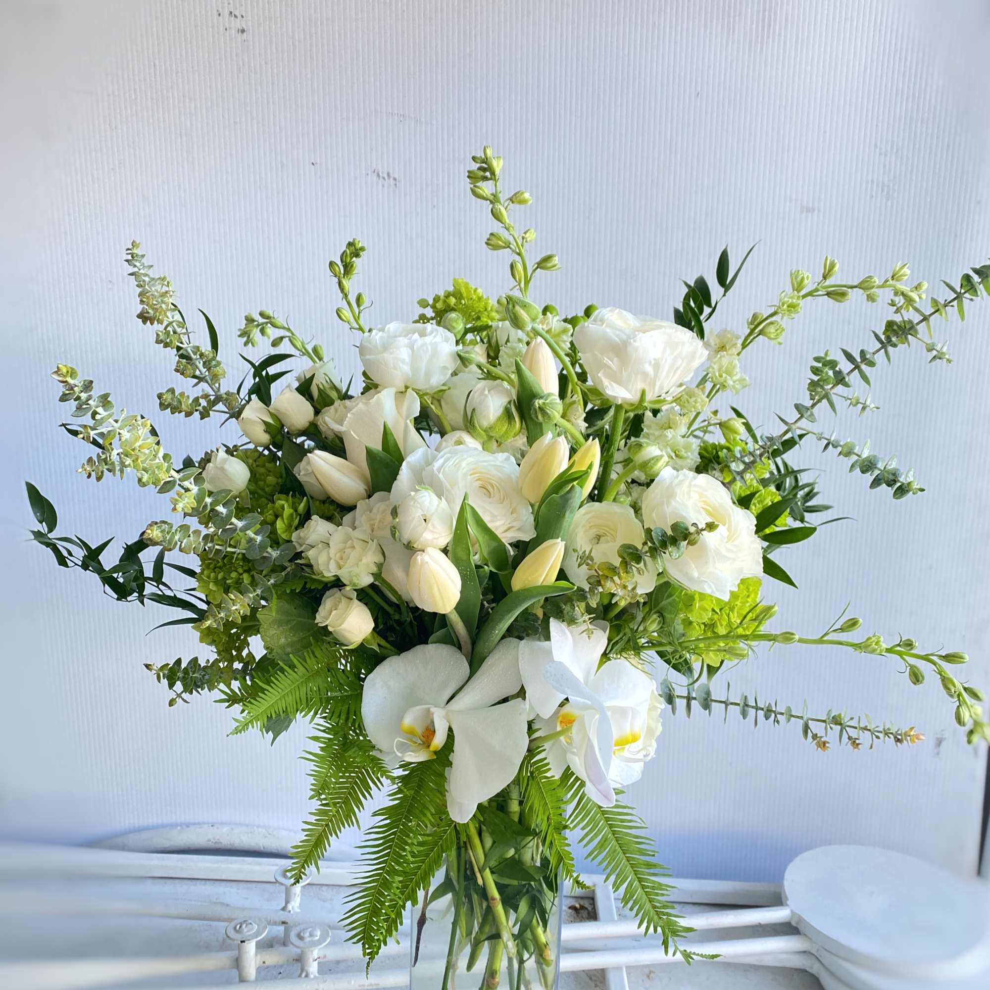 White floral arrangement in a clear glass vase with orchids and tulips