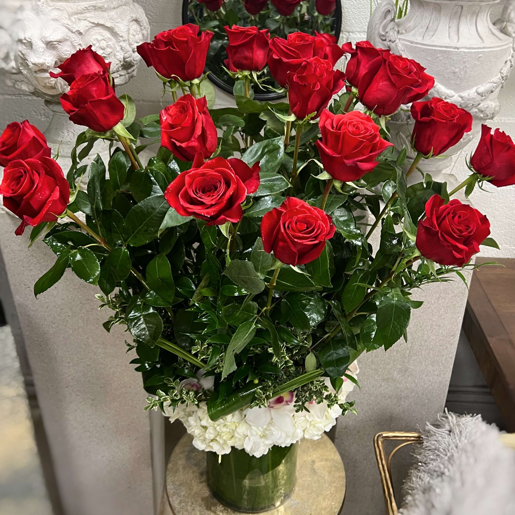 Red roses arranged in a clear vase with white flowers at the base