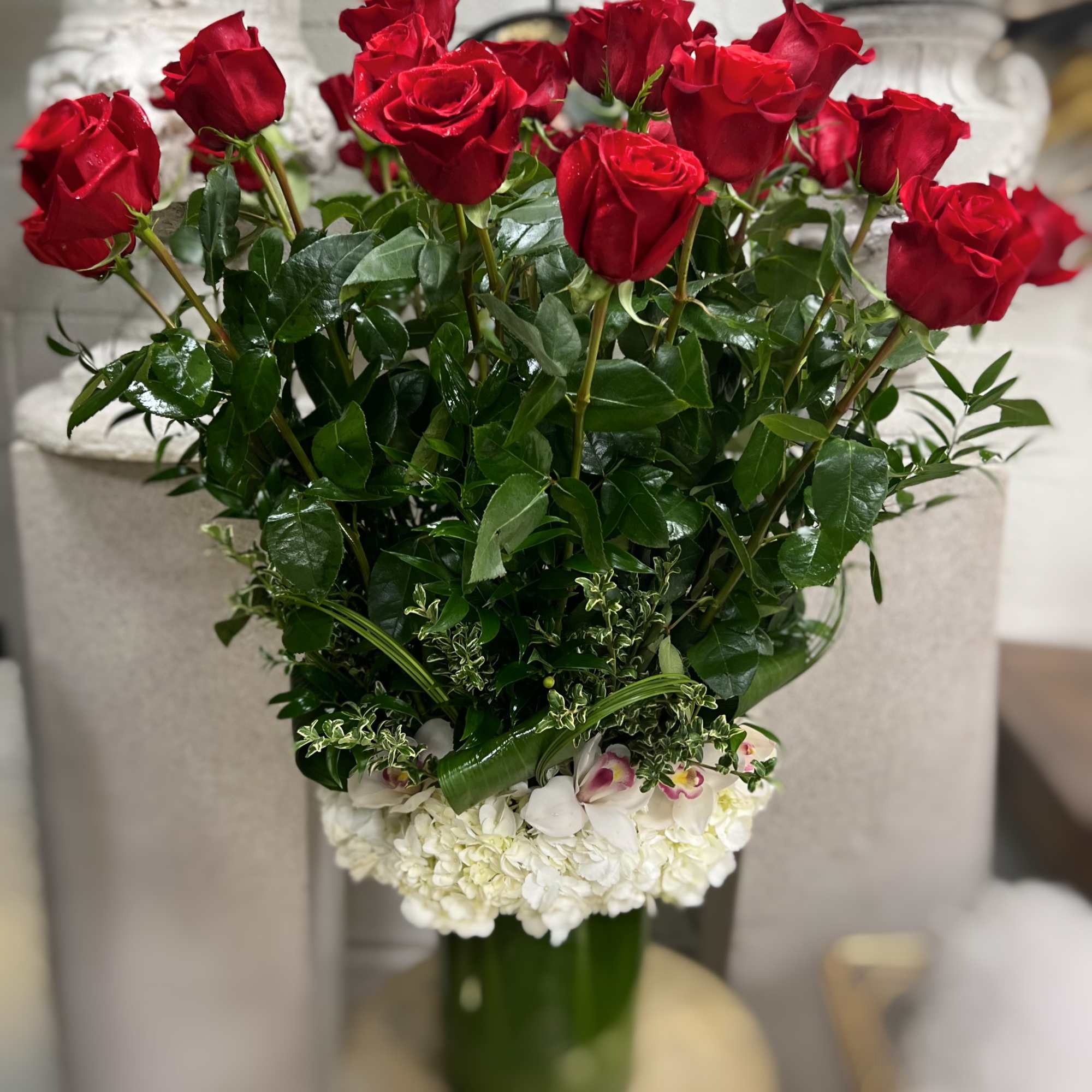 Red roses arranged in a tall vase with white flowers at the base