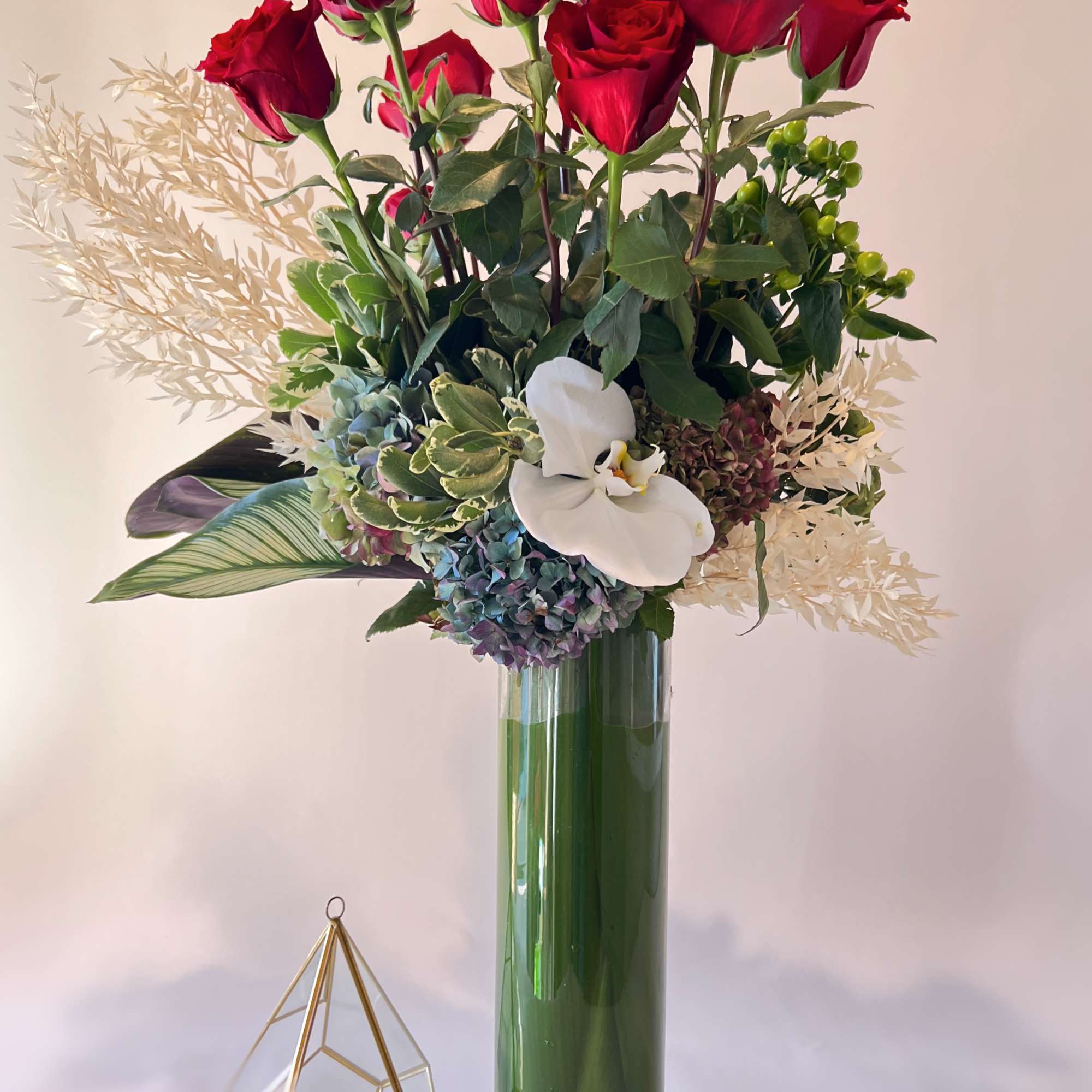 Red roses and a white orchid in a tall glass vase