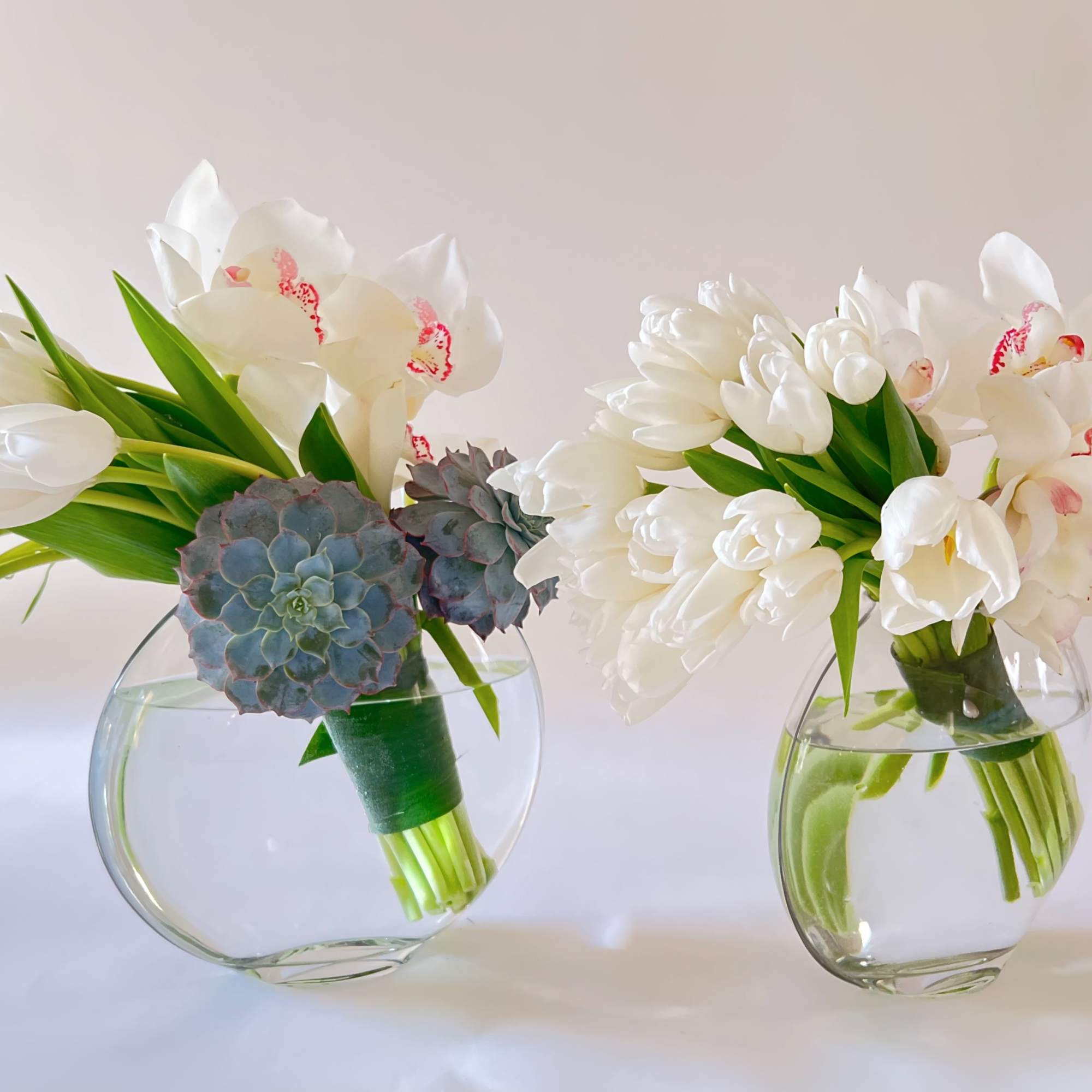 Two white floral bouquets in clear glass vases with succulents