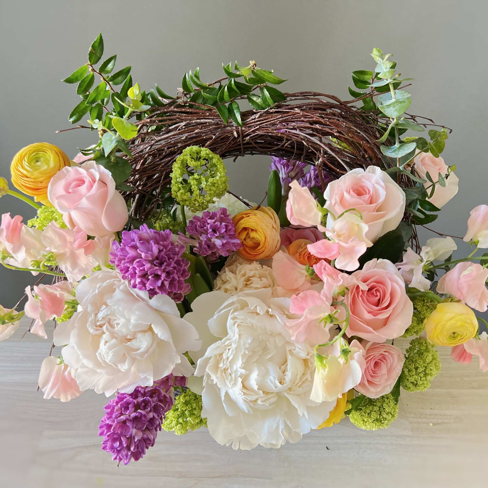Mixed bouquet with pink and white roses, purple blooms, and yellow flowers in a twig wreath