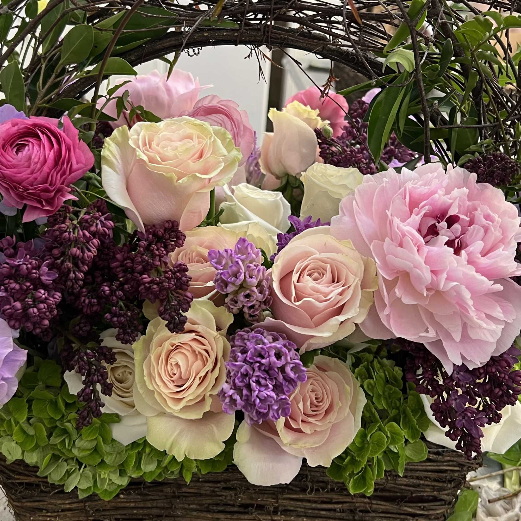 Basket arrangement of pink and lavender roses with peonies and lilac