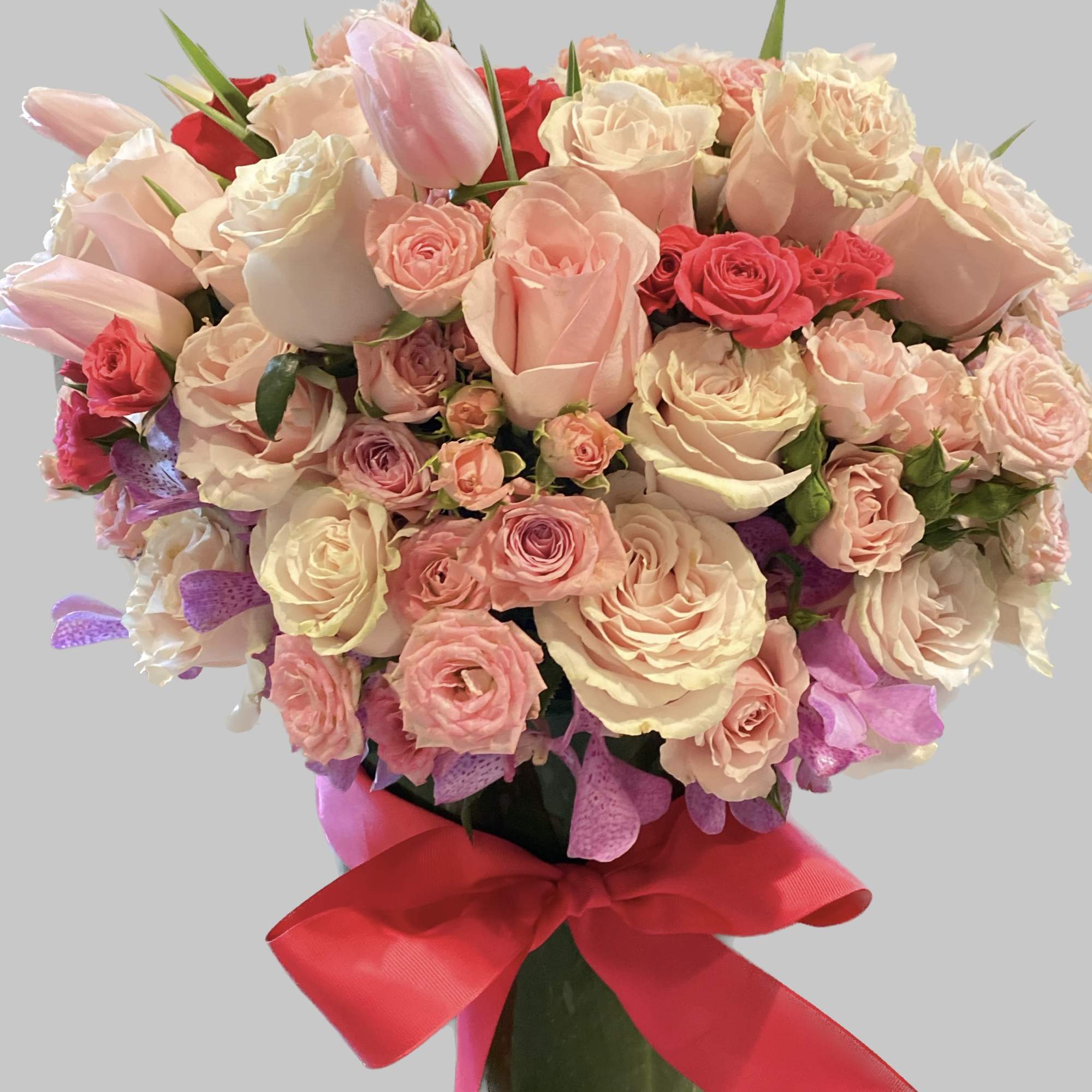 Bouquet of pink and cream roses with tulips tied with a red ribbon