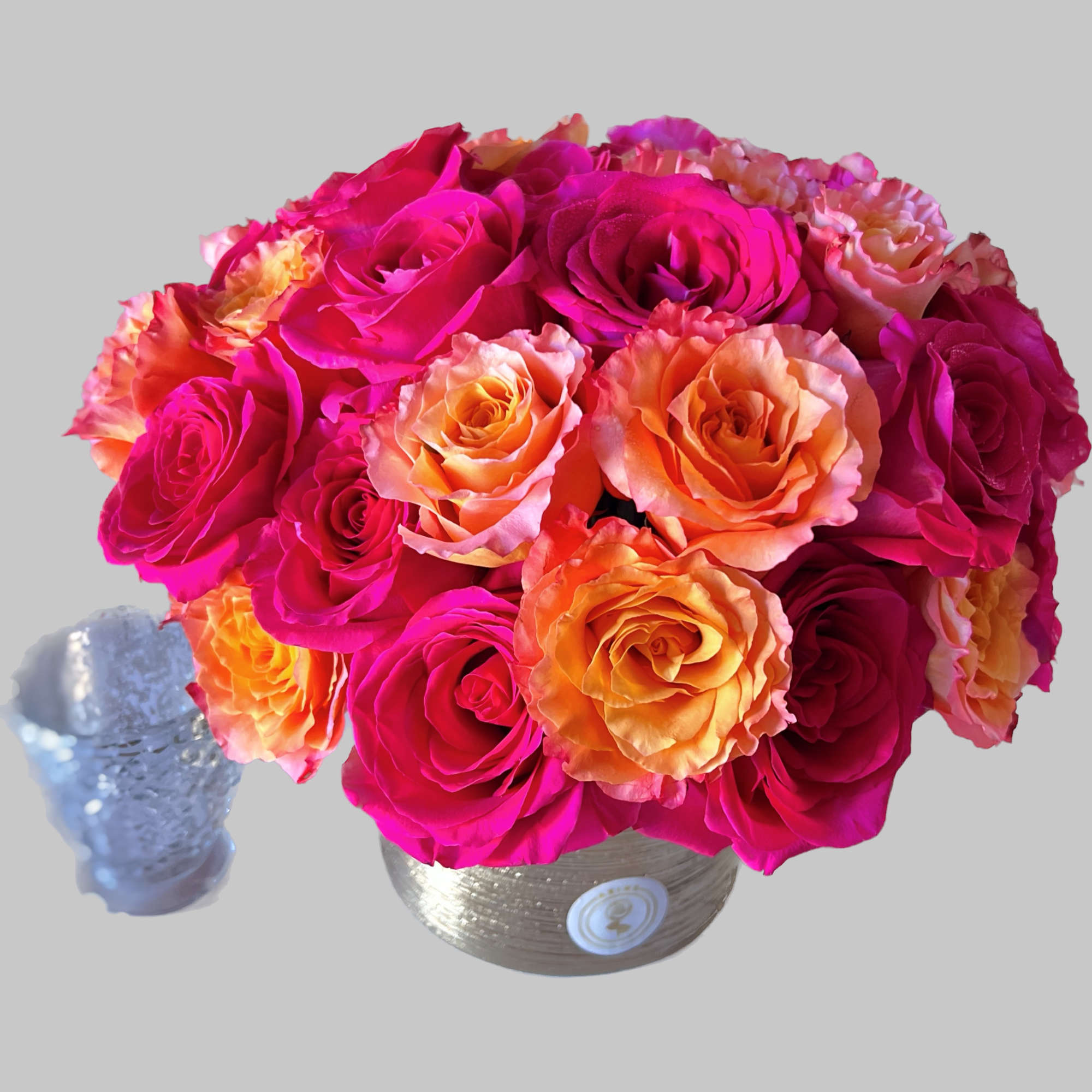 Bouquet of pink and orange roses in a metallic vase with a small candle