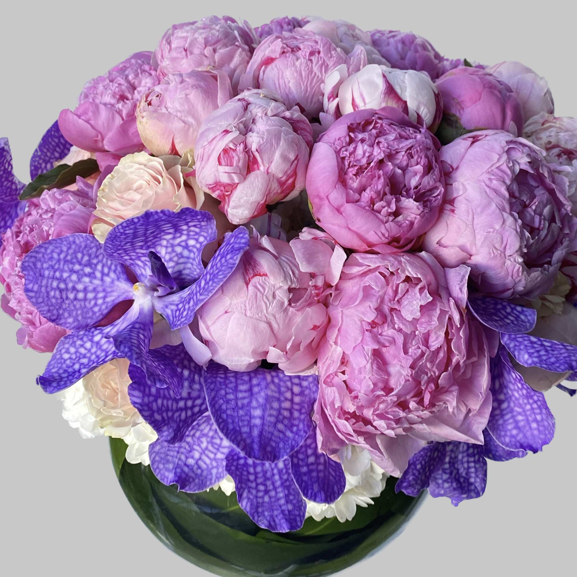 Pink peonies and purple orchids arranged in a glass vase