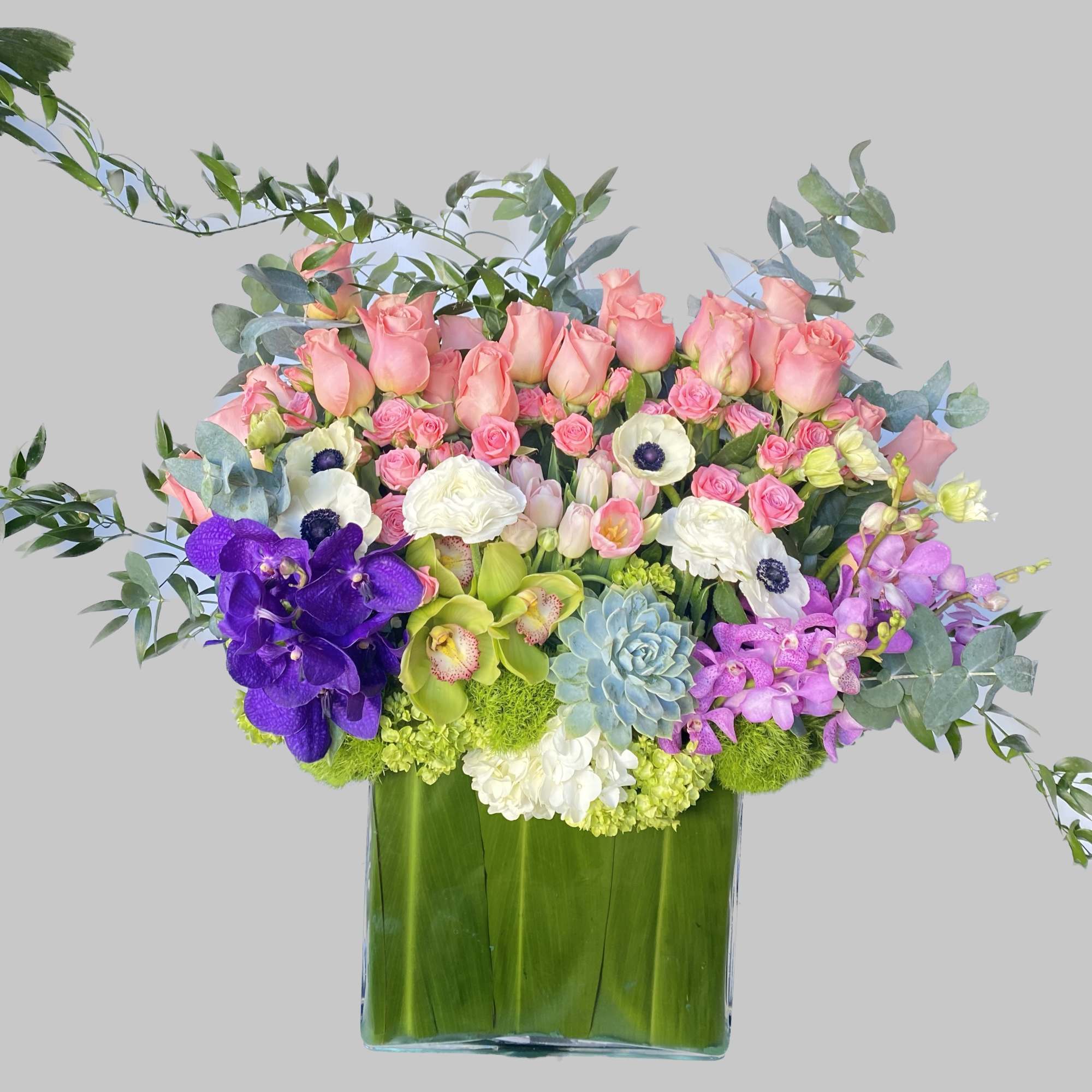 Large mixed bouquet of pink roses, orchids, and white blooms in a glass vase