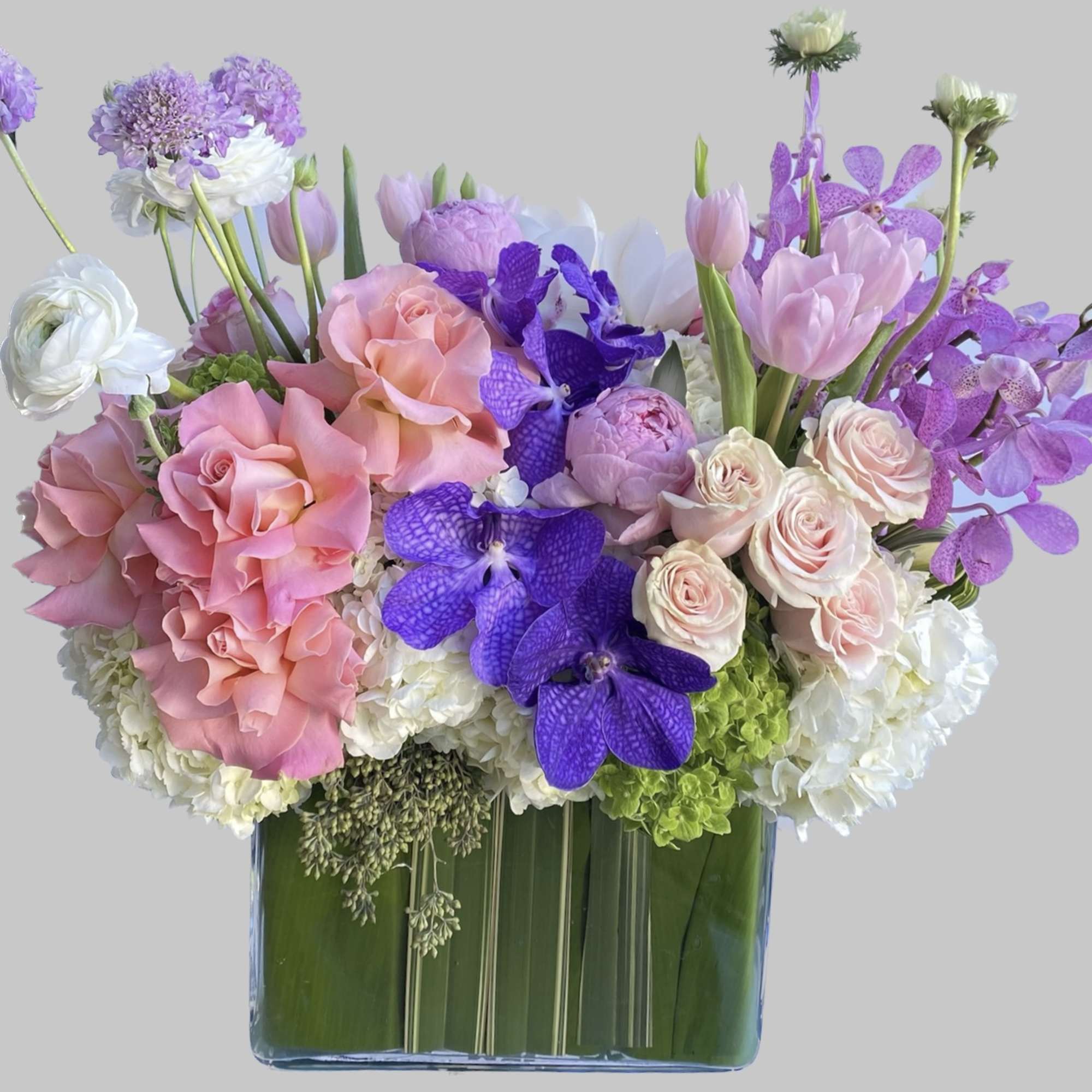Pink roses and purple orchids arranged in a square glass vase
