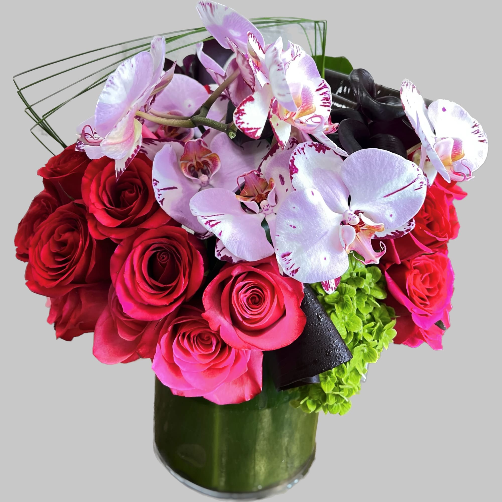 Bouquet of red roses and pink orchids in a green glass vase
