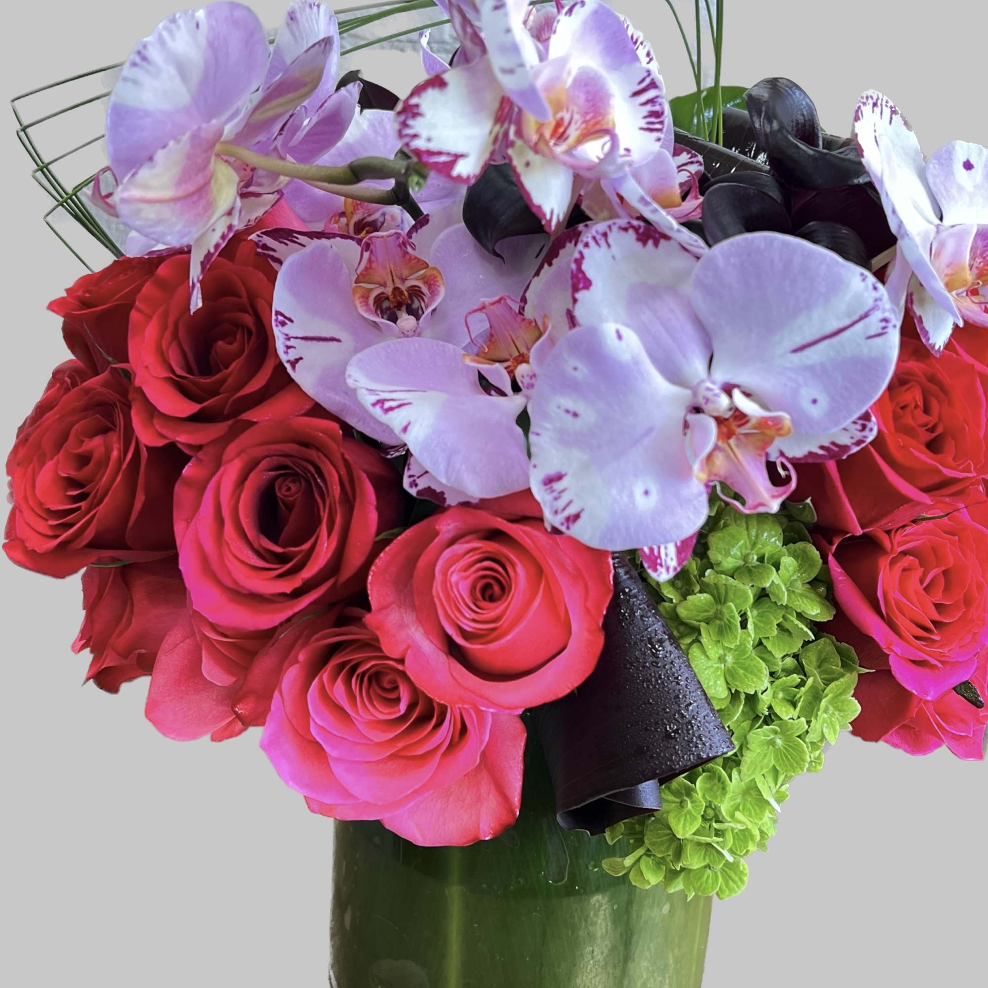 Bouquet of red roses and pink orchids in a green vase