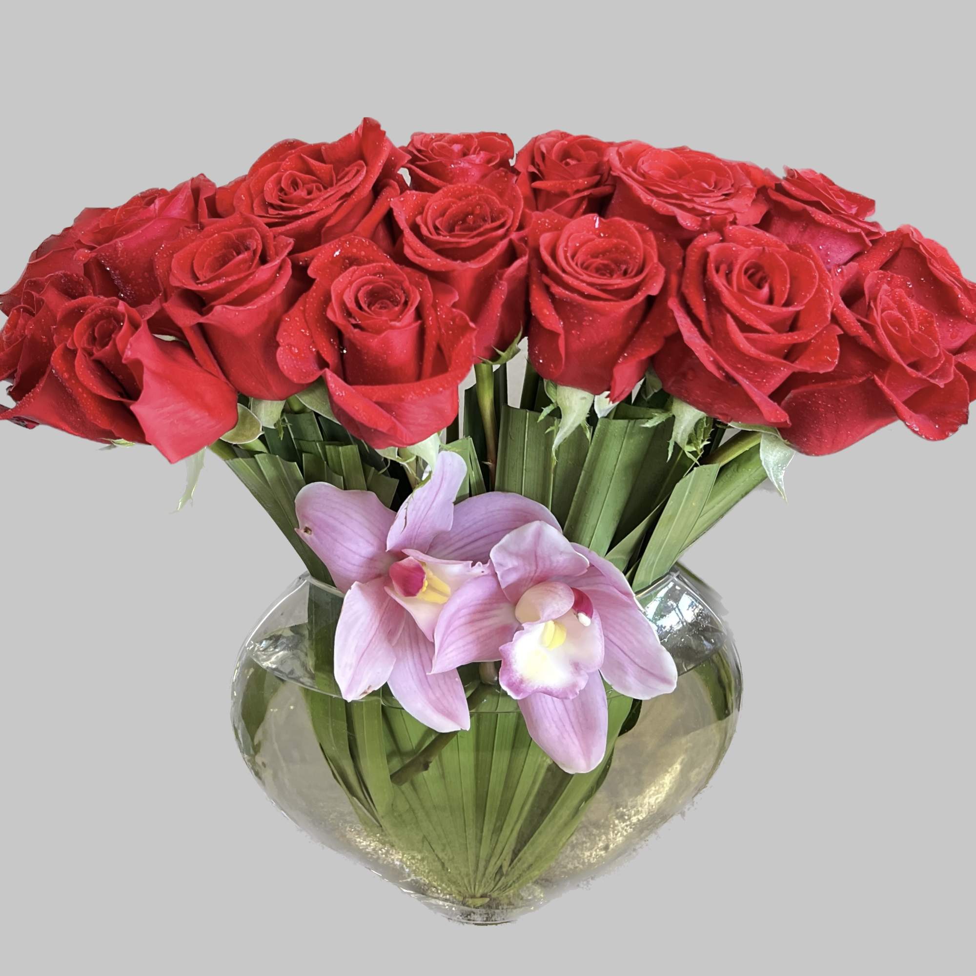 Red roses and pink orchids arranged in a clear glass vase