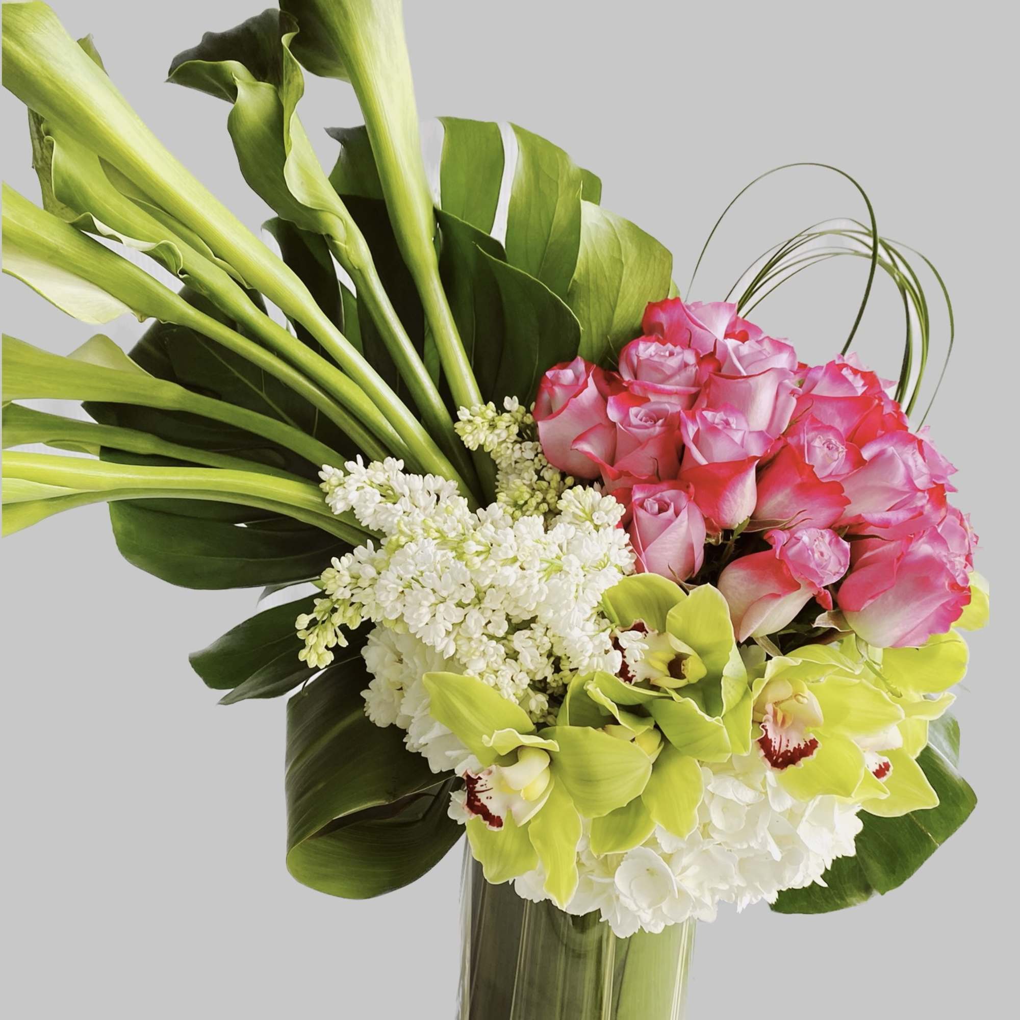 Bouquet of pink roses, green orchids, and white flowers in a tall vase