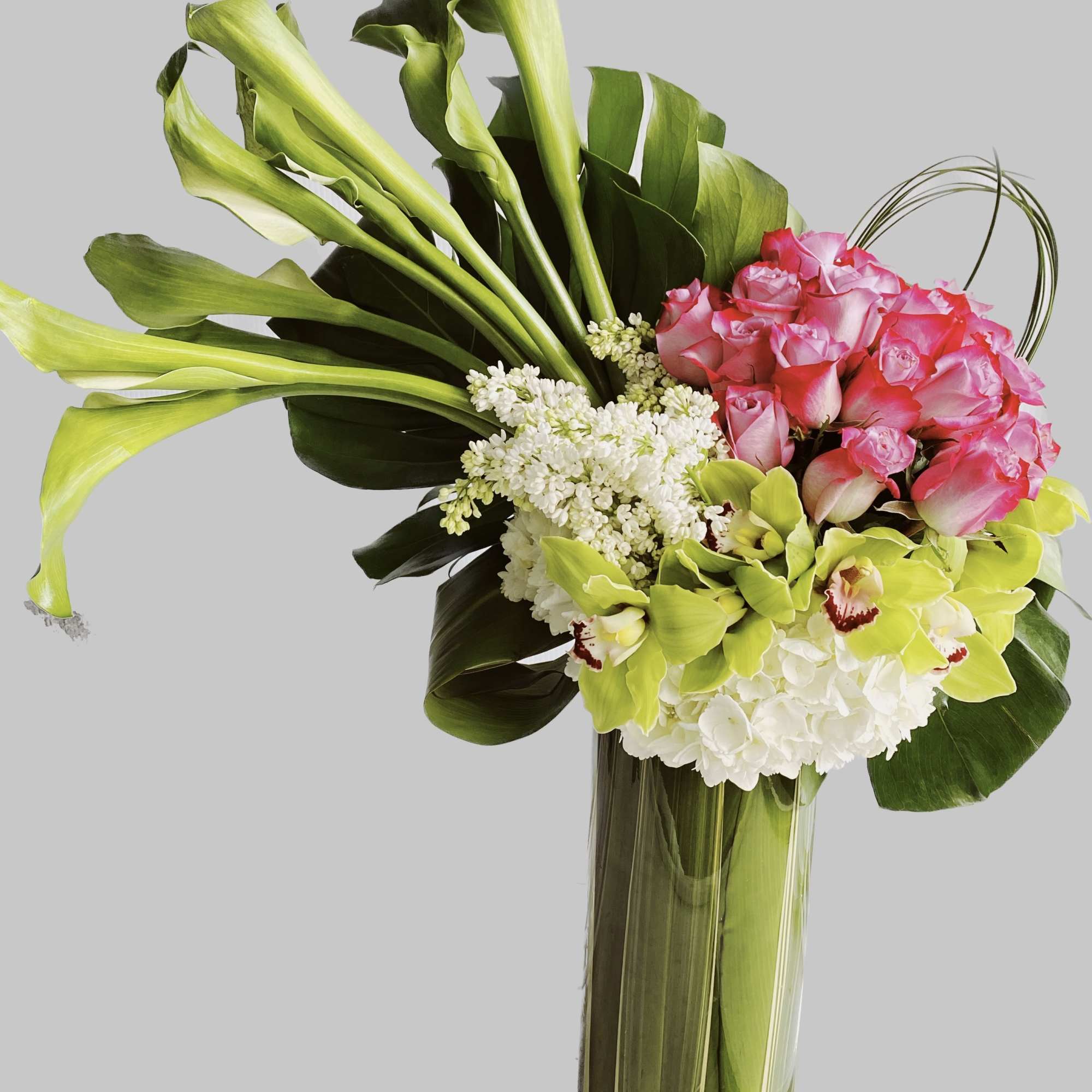 Pink roses and green calla lilies in a tall glass vase