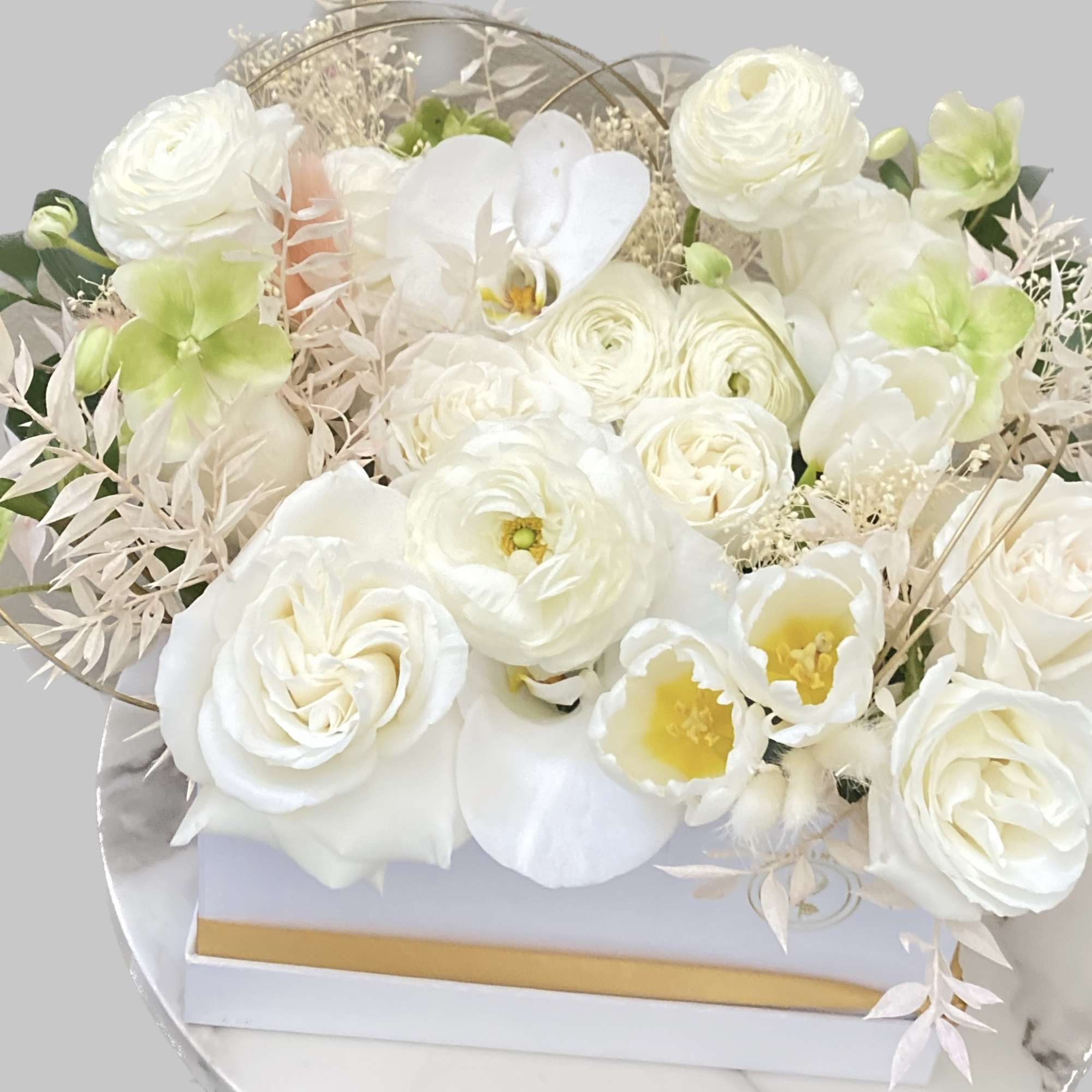 White floral arrangement with roses and orchids in a round box