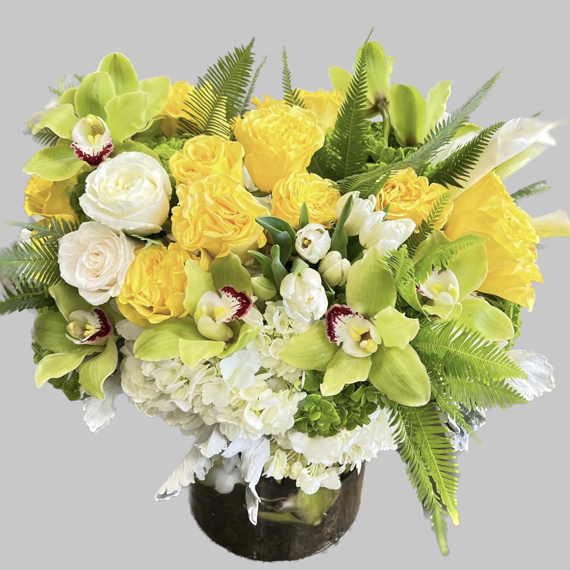 Yellow and white floral arrangement in a dark vase with green orchids