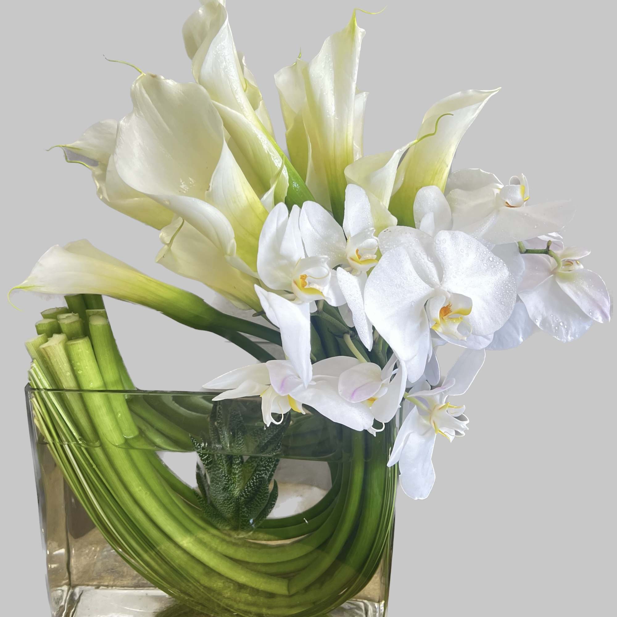 White calla lilies and orchids in a square glass vase