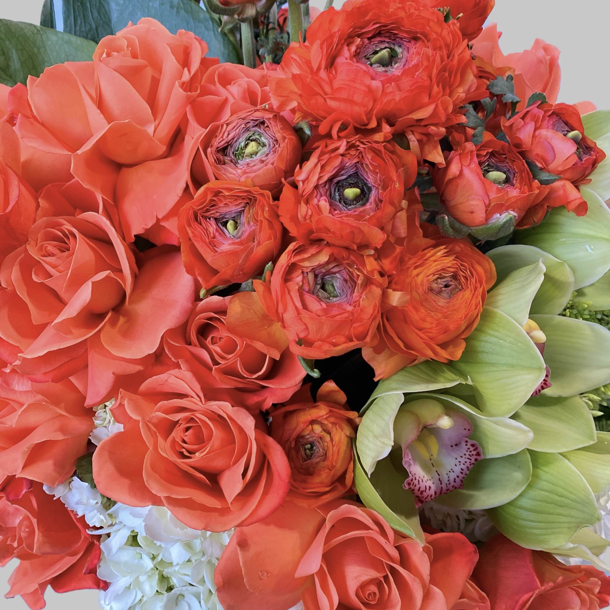 Coral roses and orange ranunculus with pale green orchids in a bouquet