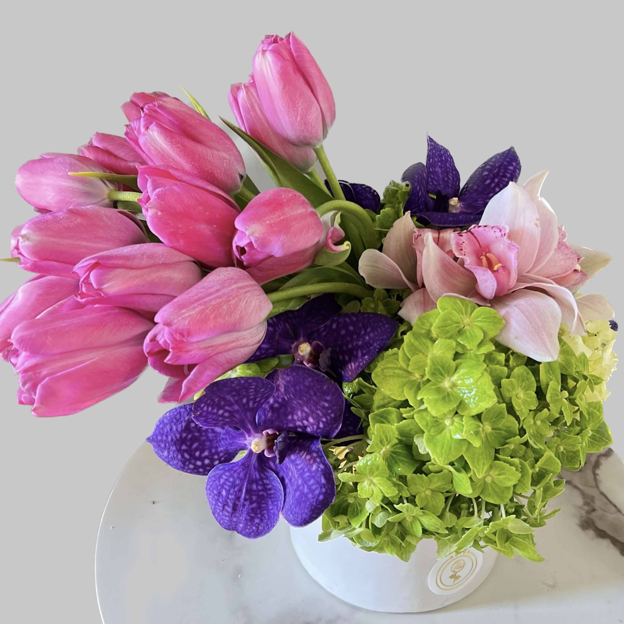 Pink tulips, purple orchids, and green hydrangeas in a white vase