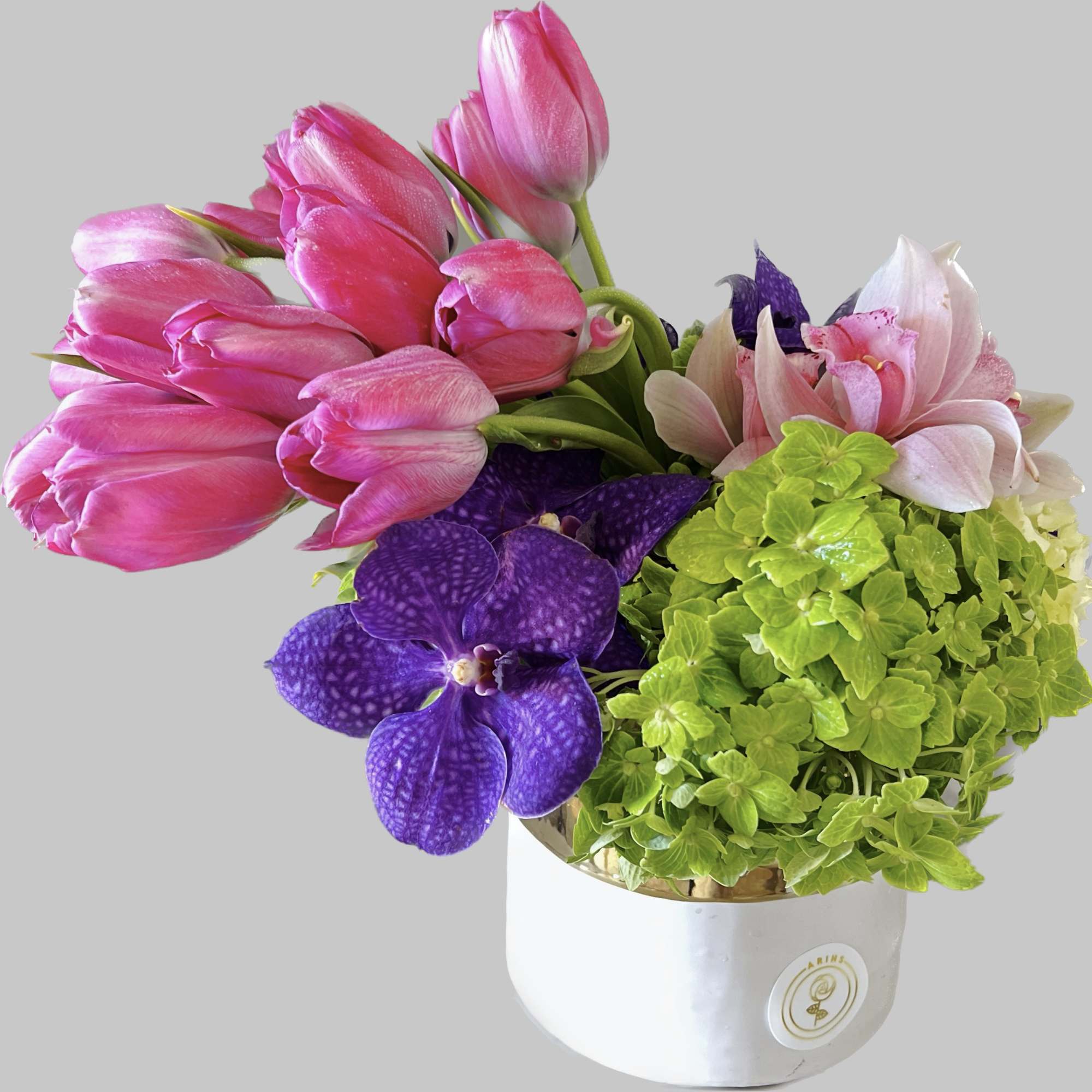 Pink tulips and purple orchids in a white hatbox with green hydrangea