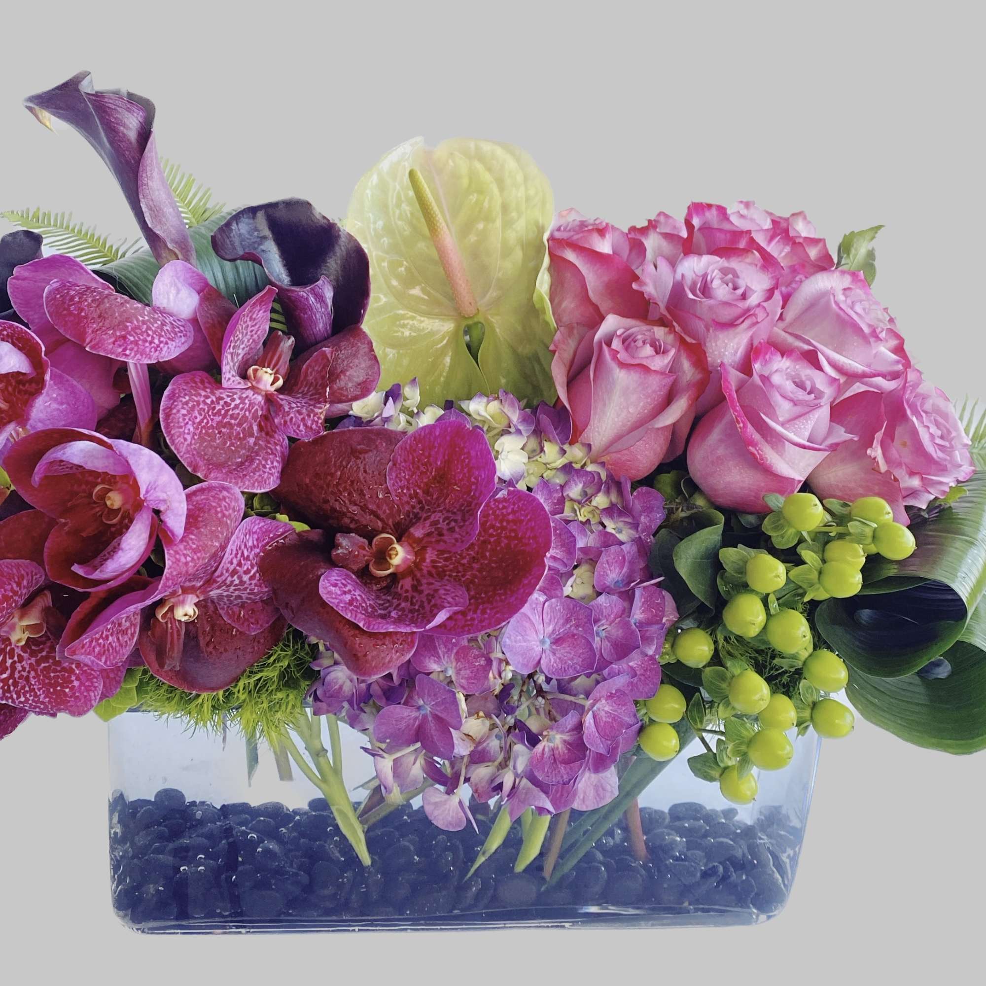 Pink roses and purple orchids in a clear rectangular vase