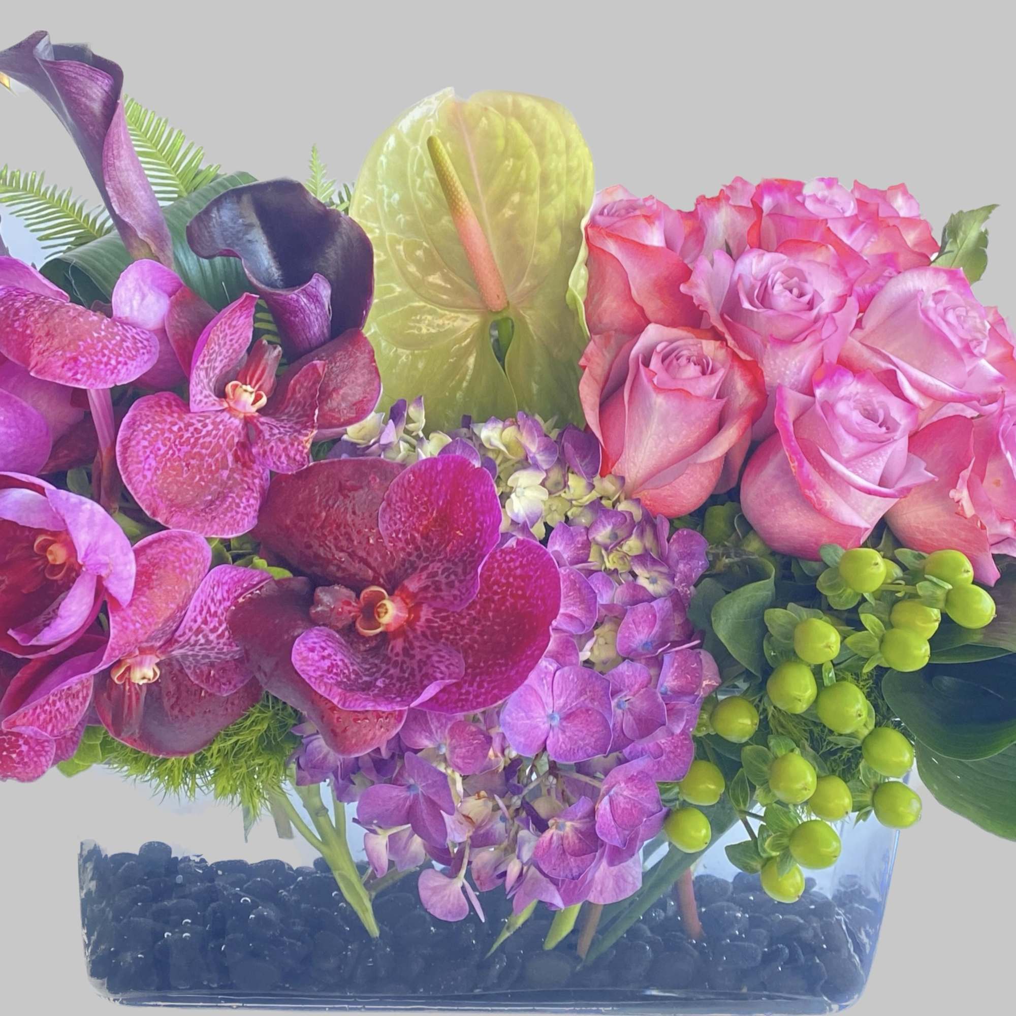 Pink roses and purple orchids arranged in a clear rectangular vase