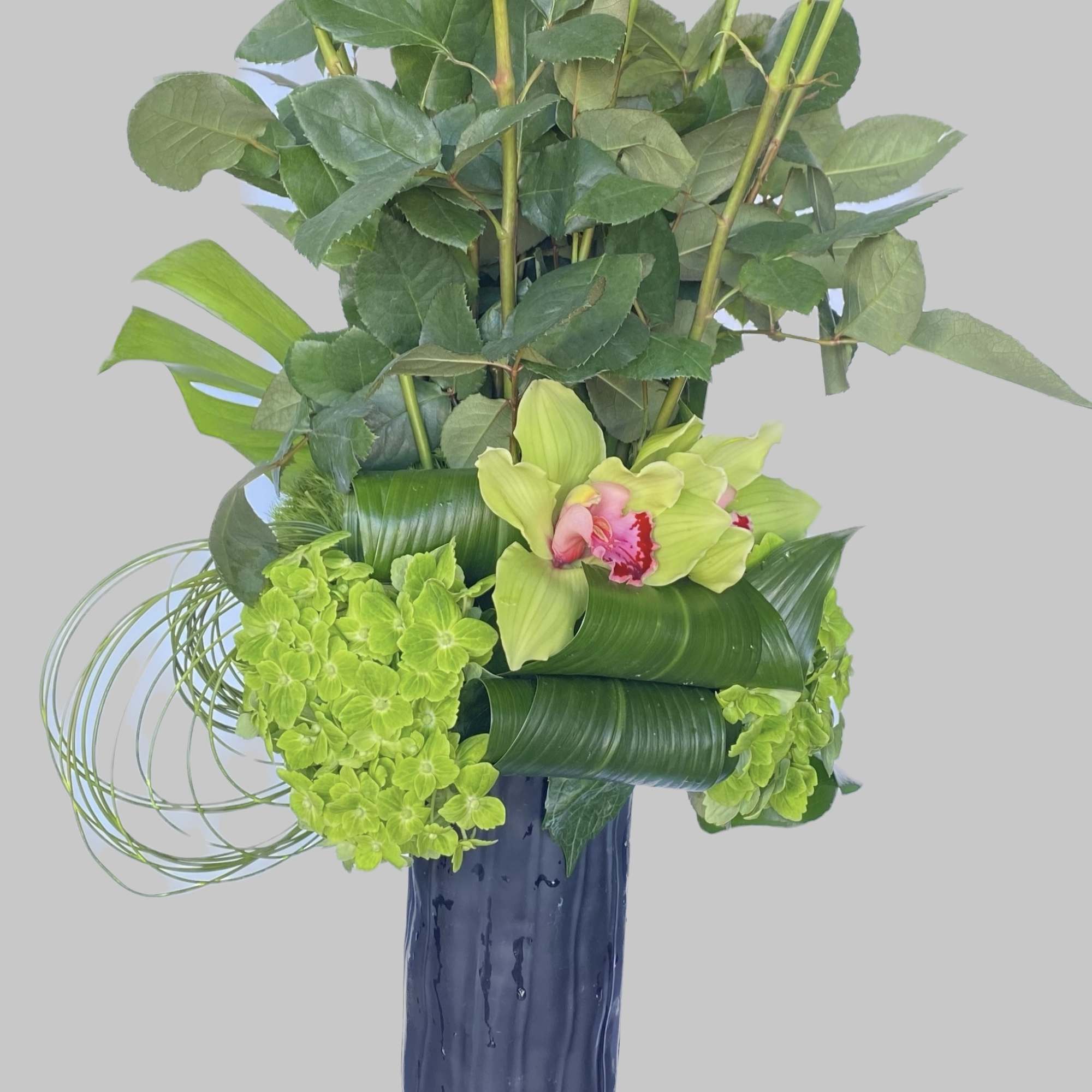 Tall arrangement of red roses and green orchids in a blue vase