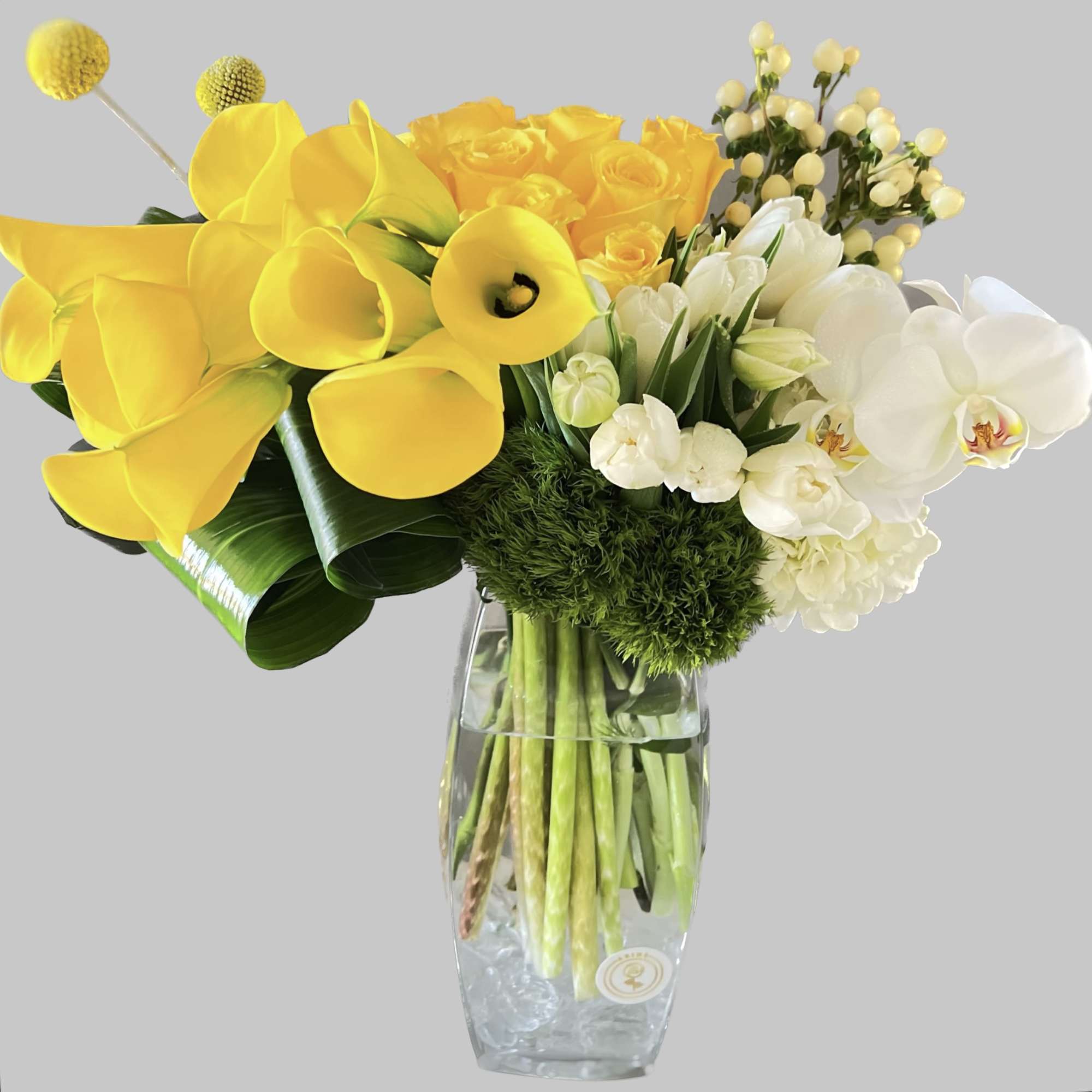 Yellow calla lilies, roses, and white orchids in a glass vase
