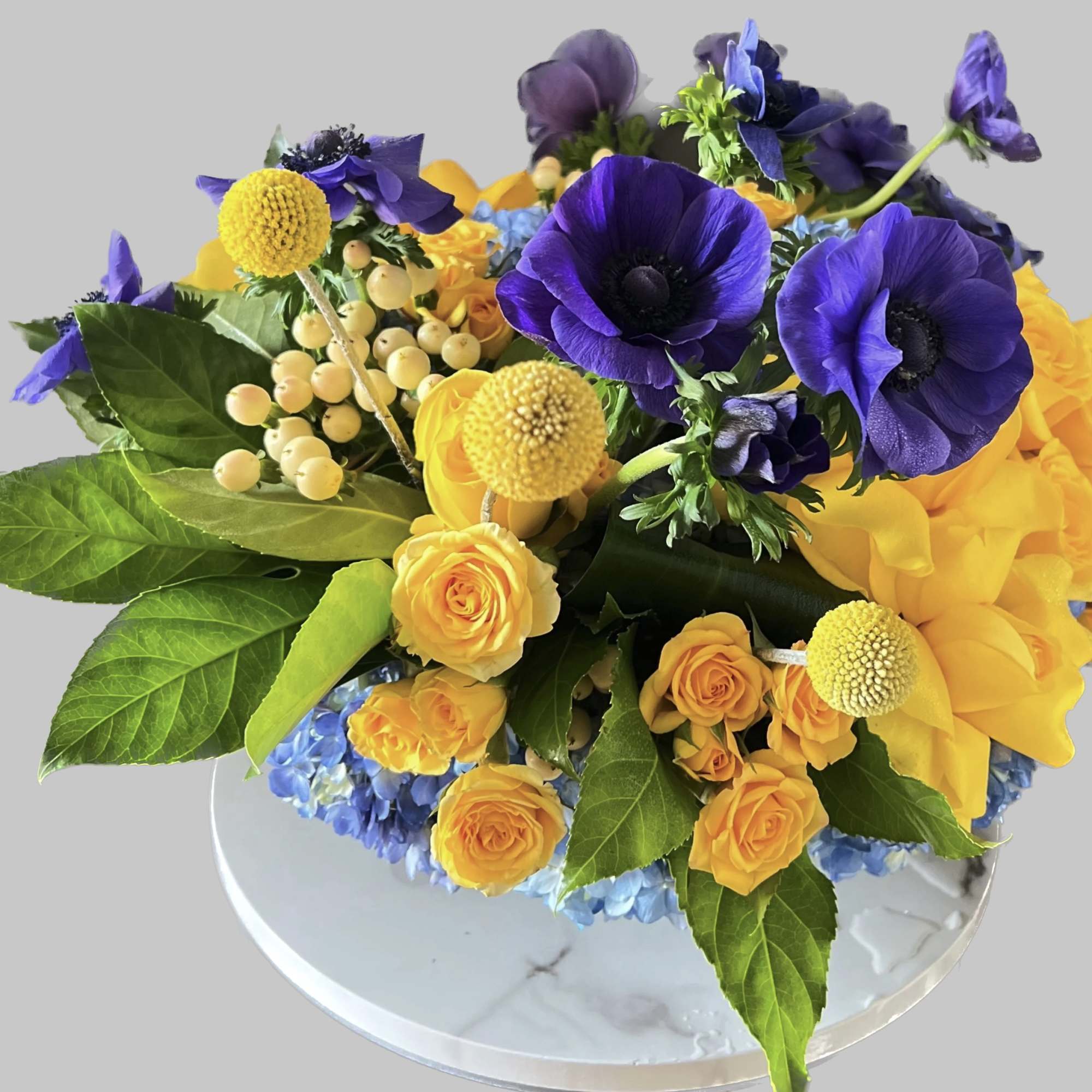 Purple anemones and yellow roses in a low round arrangement