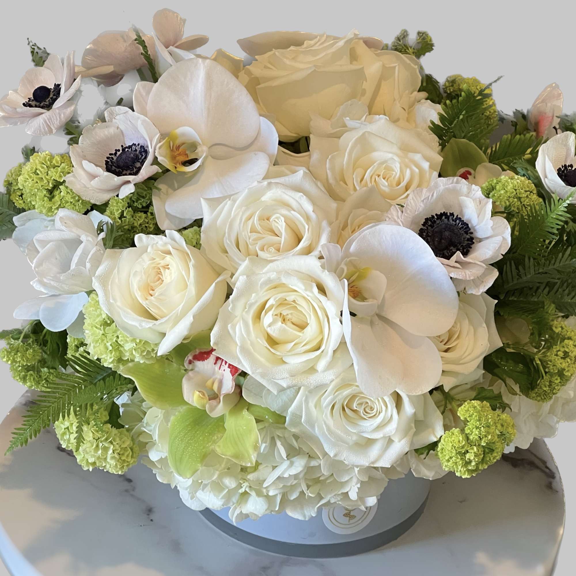 White rose and orchid arrangement with green accents in a round box