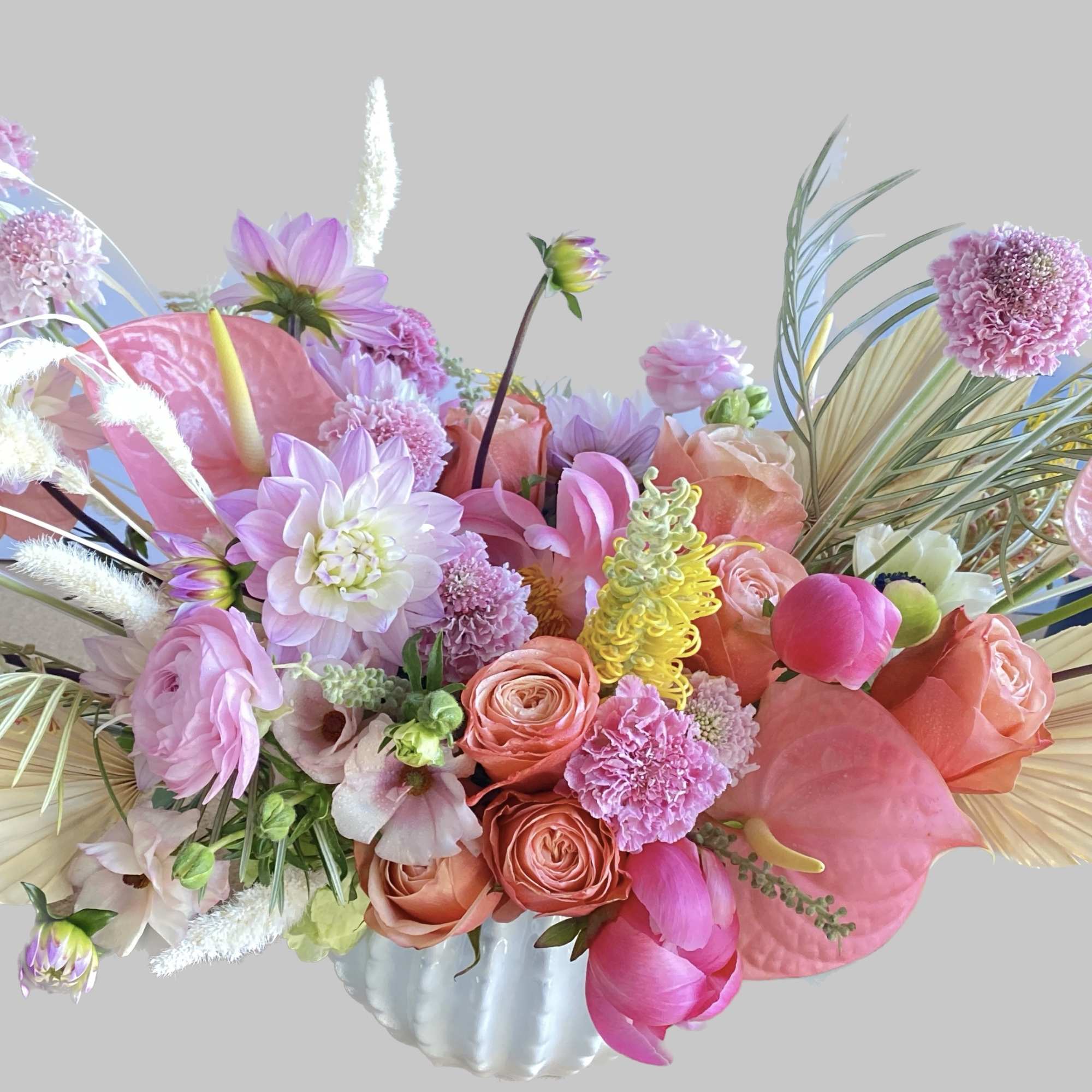 Pink and peach floral arrangement in a white vase with tropical leaves