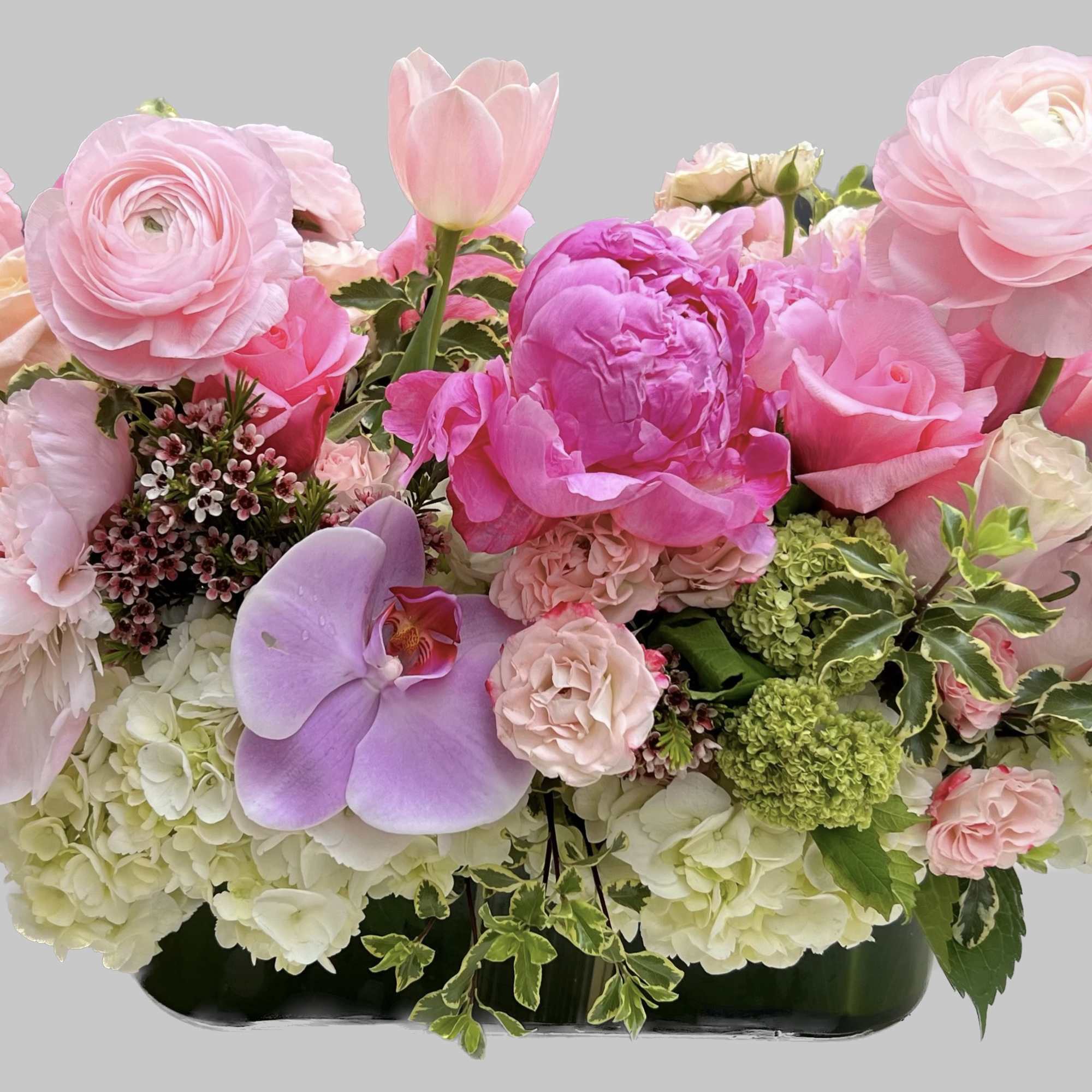 Pink floral arrangement with peonies, roses, tulips, and orchids in a low container