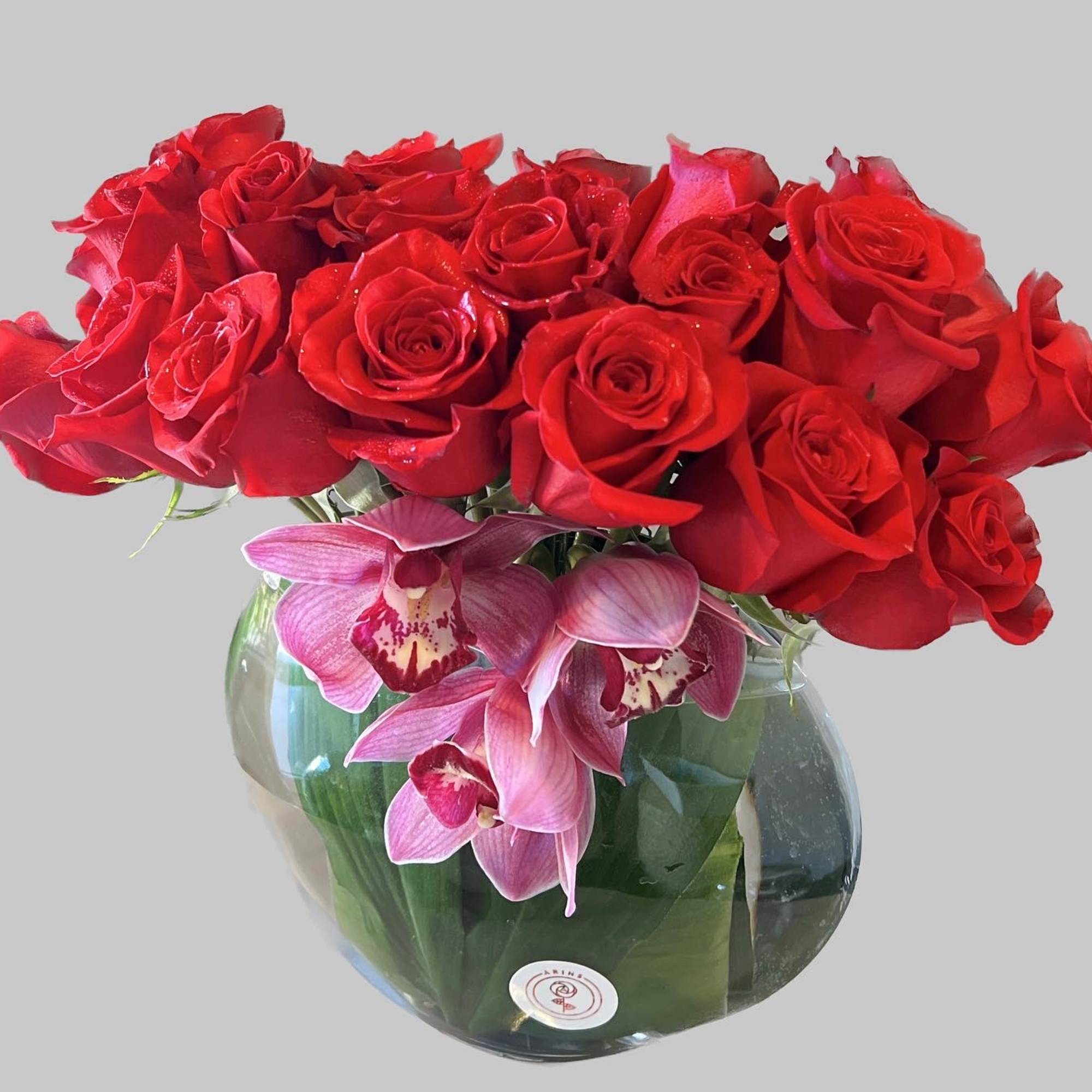 Red roses and pink orchids arranged in a round glass vase.