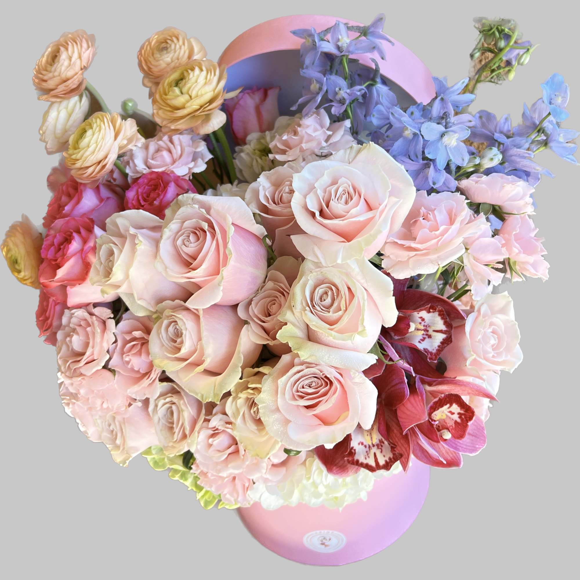 Pastel bouquet of roses, ranunculus, and blue delphinium in a pink hatbox