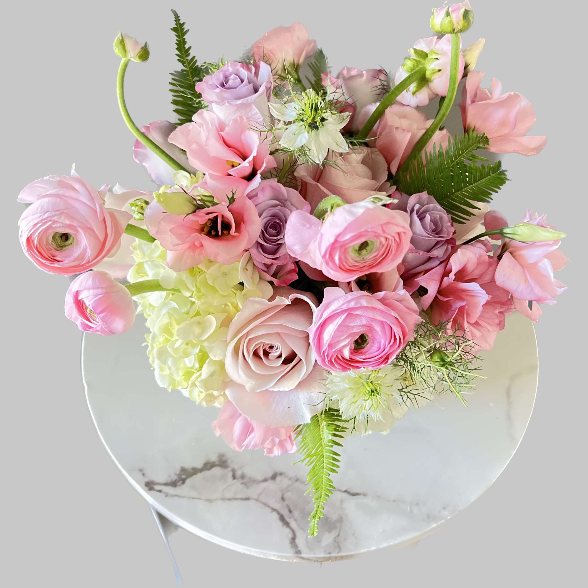 Pink and lavender bouquet with roses, ranunculus, and hydrangea in a round box
