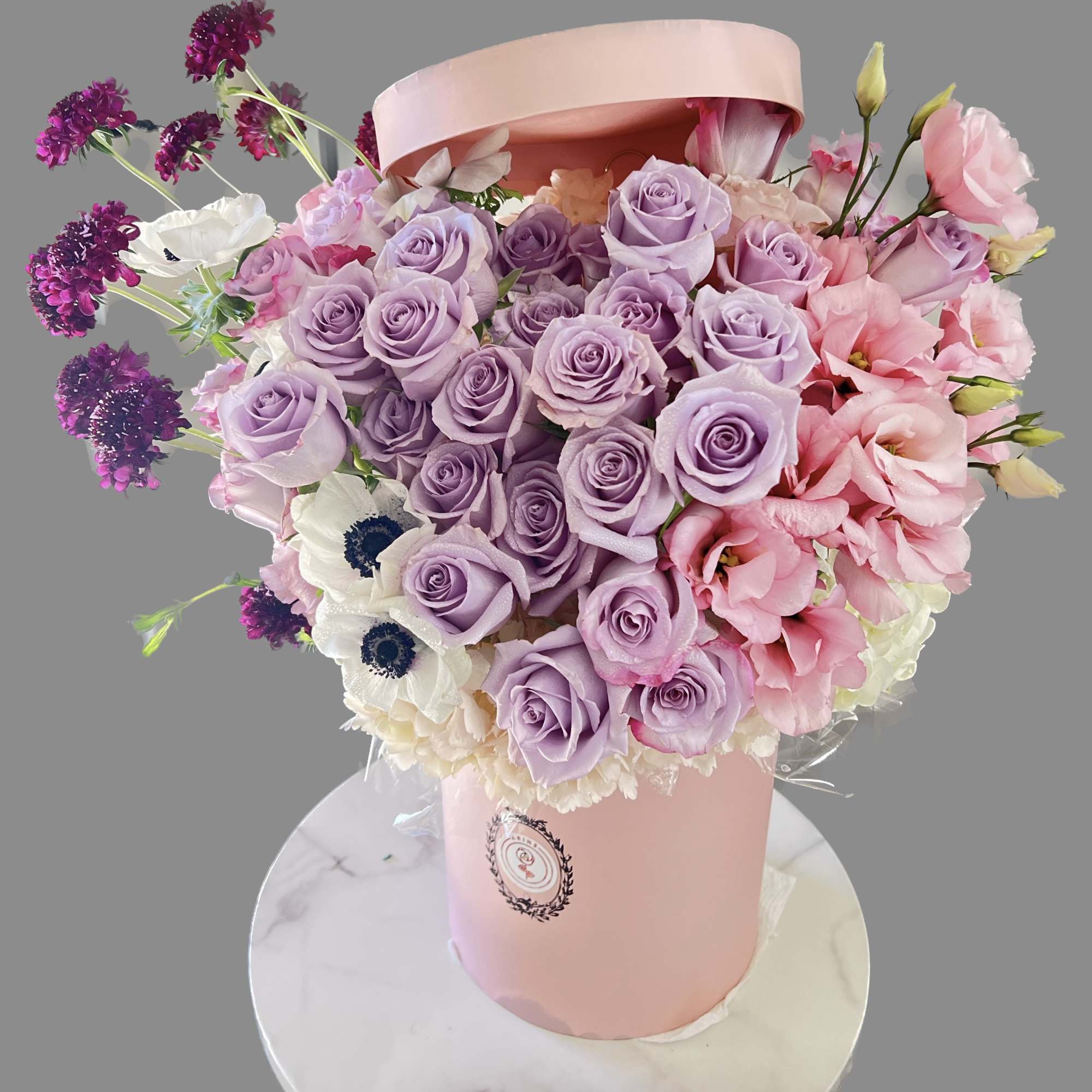 Lavender and pink rose bouquet in a pink hatbox with white flowers
