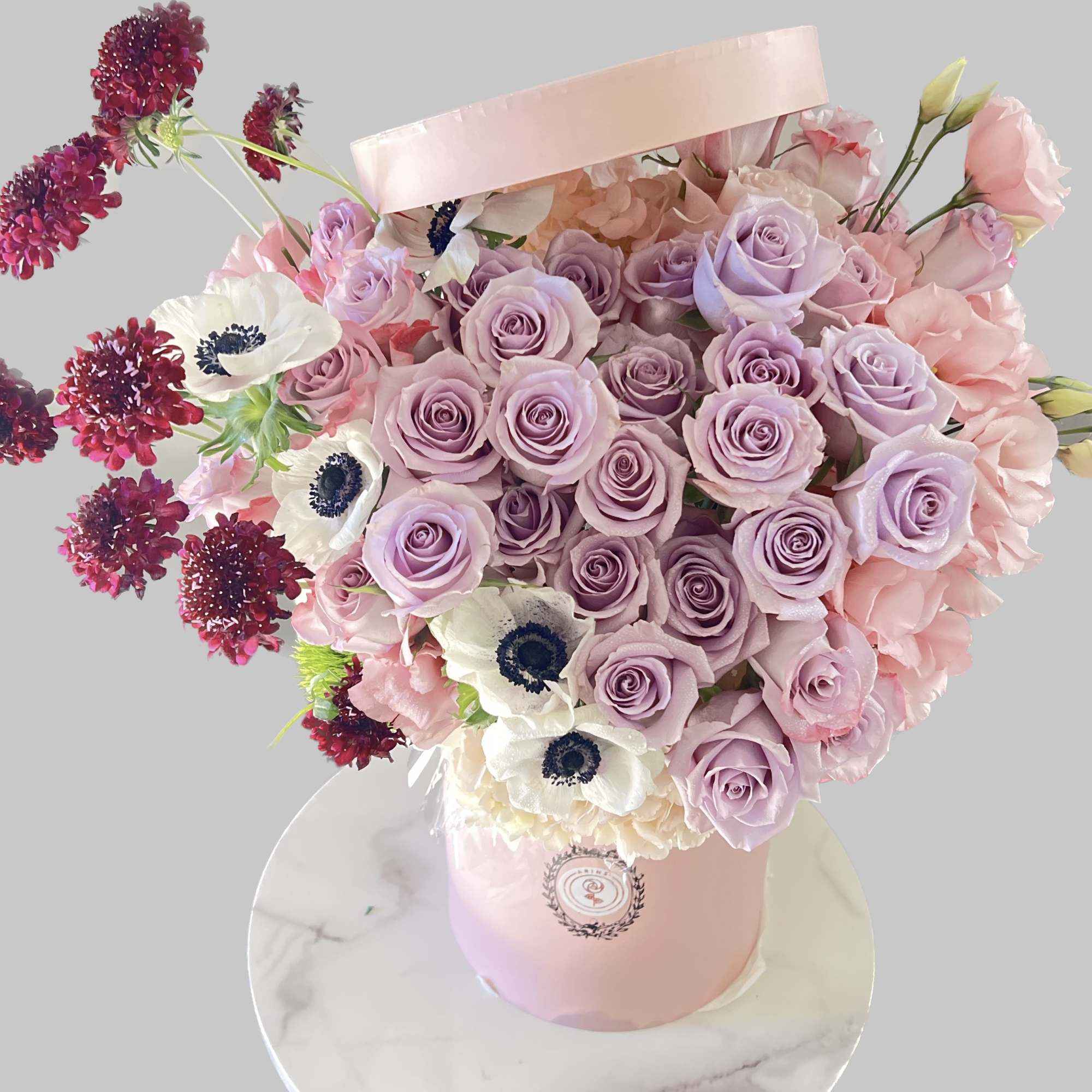 Pink and lavender rose bouquet with white anemones in a pink hatbox