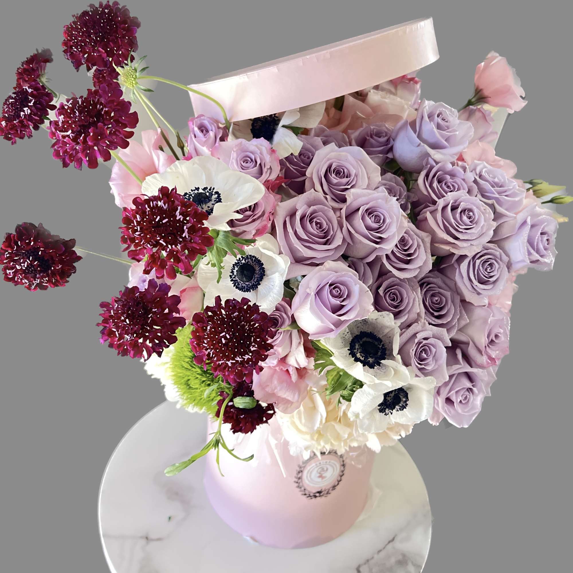 Lavender roses and white anemones in a pink hatbox with burgundy accents