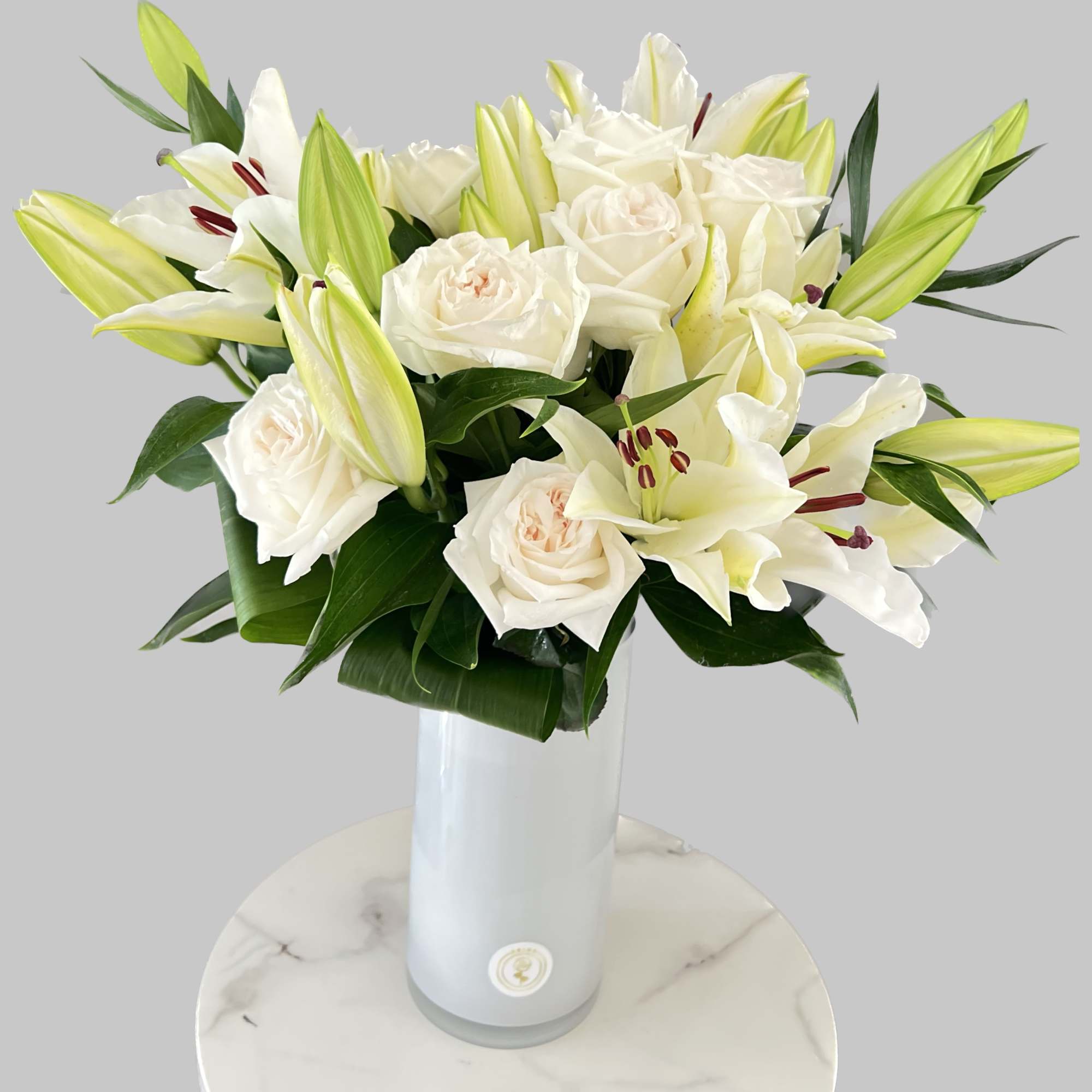 White roses and lilies arranged in a tall white vase