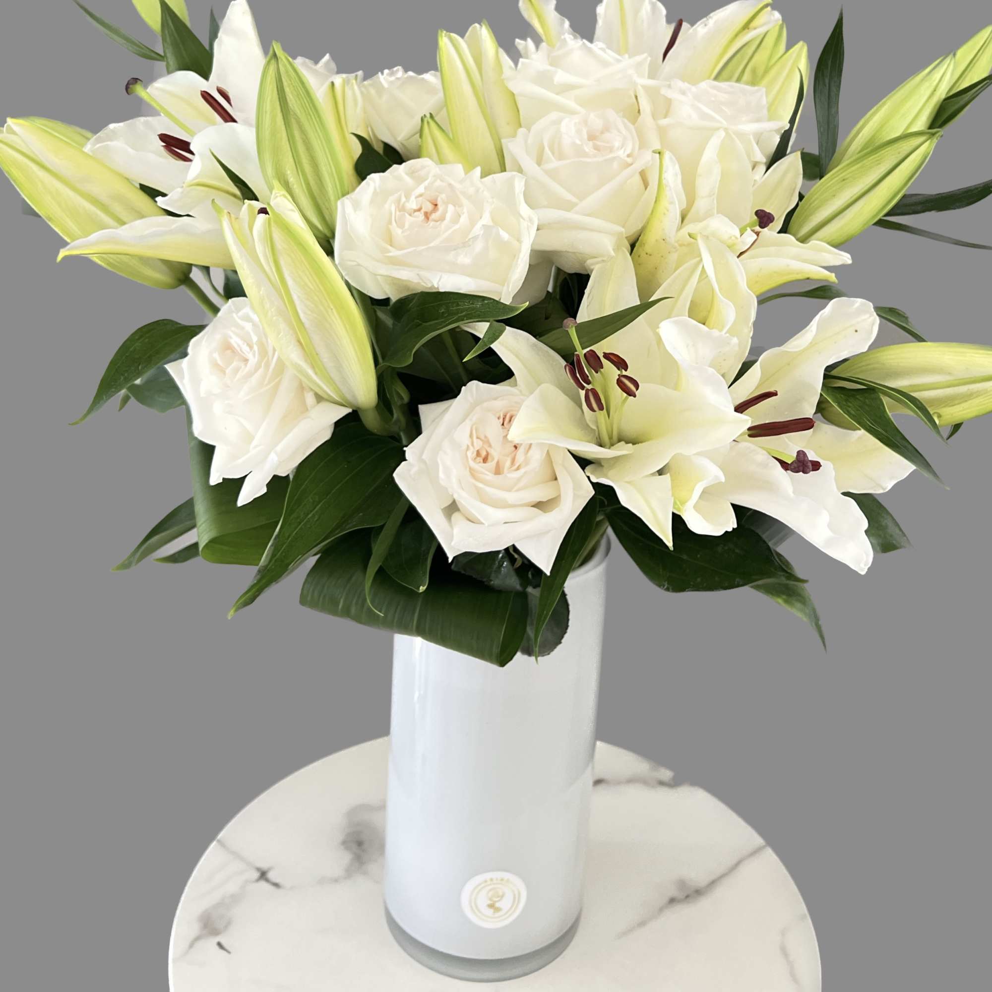 White roses and lilies arranged in a tall white vase.
