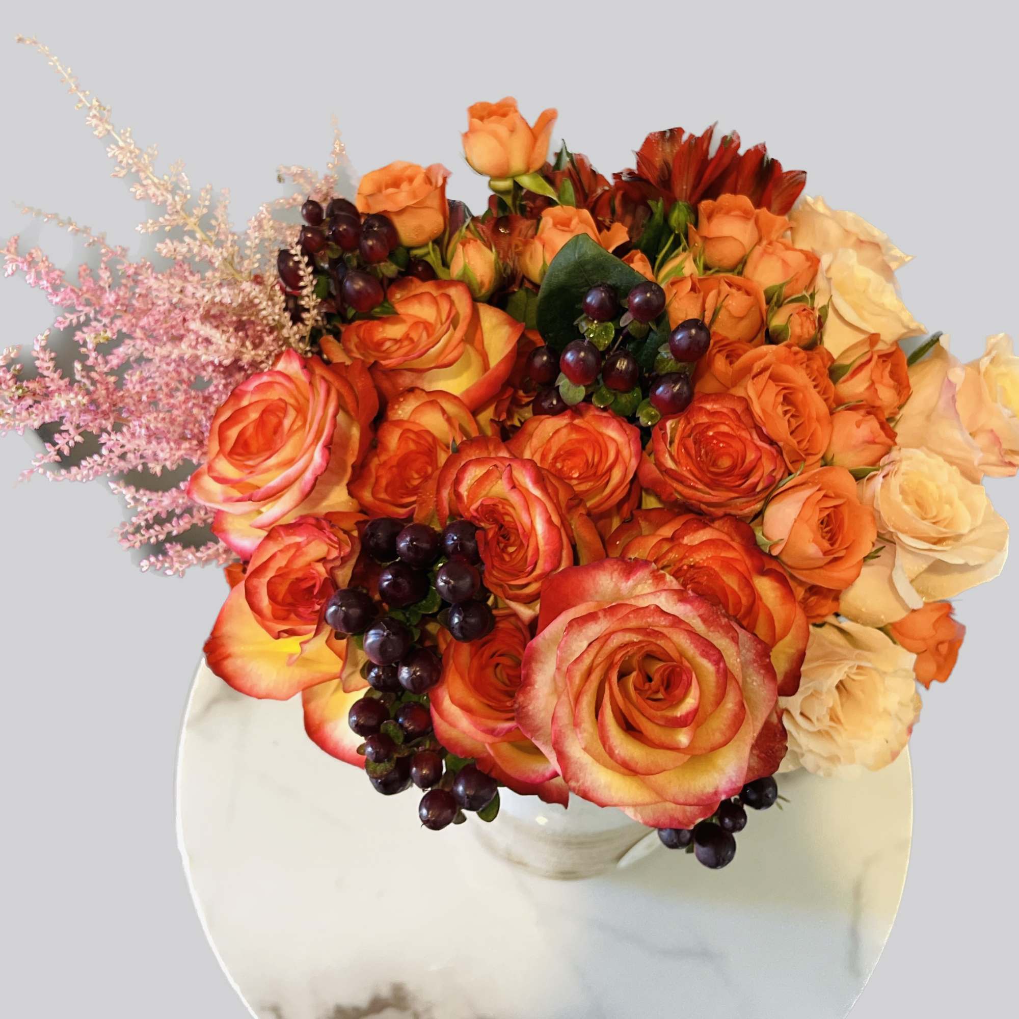 Bouquet of orange and cream roses with dark berries in a white vase