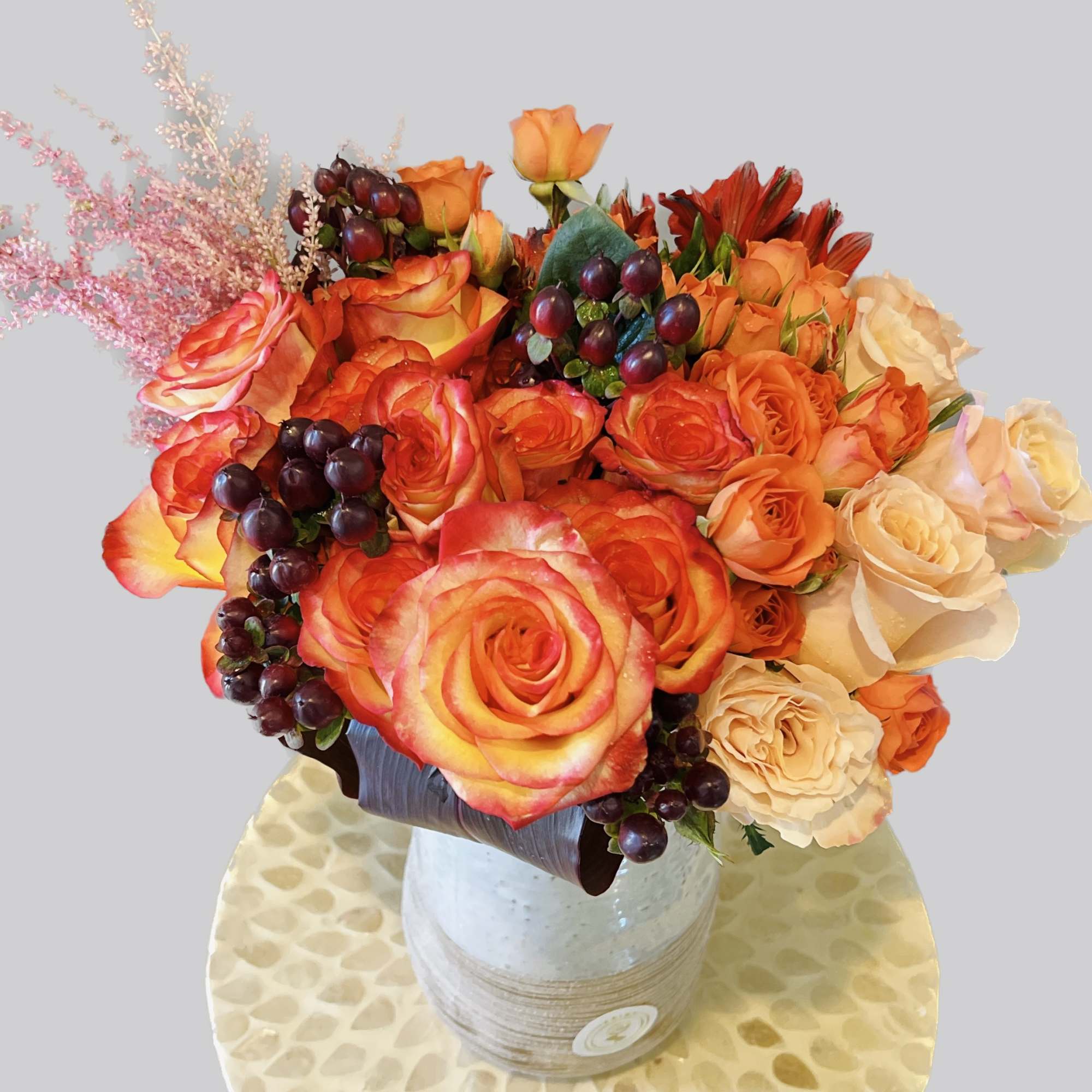 Orange and cream roses in a ceramic vase with dark berry accents