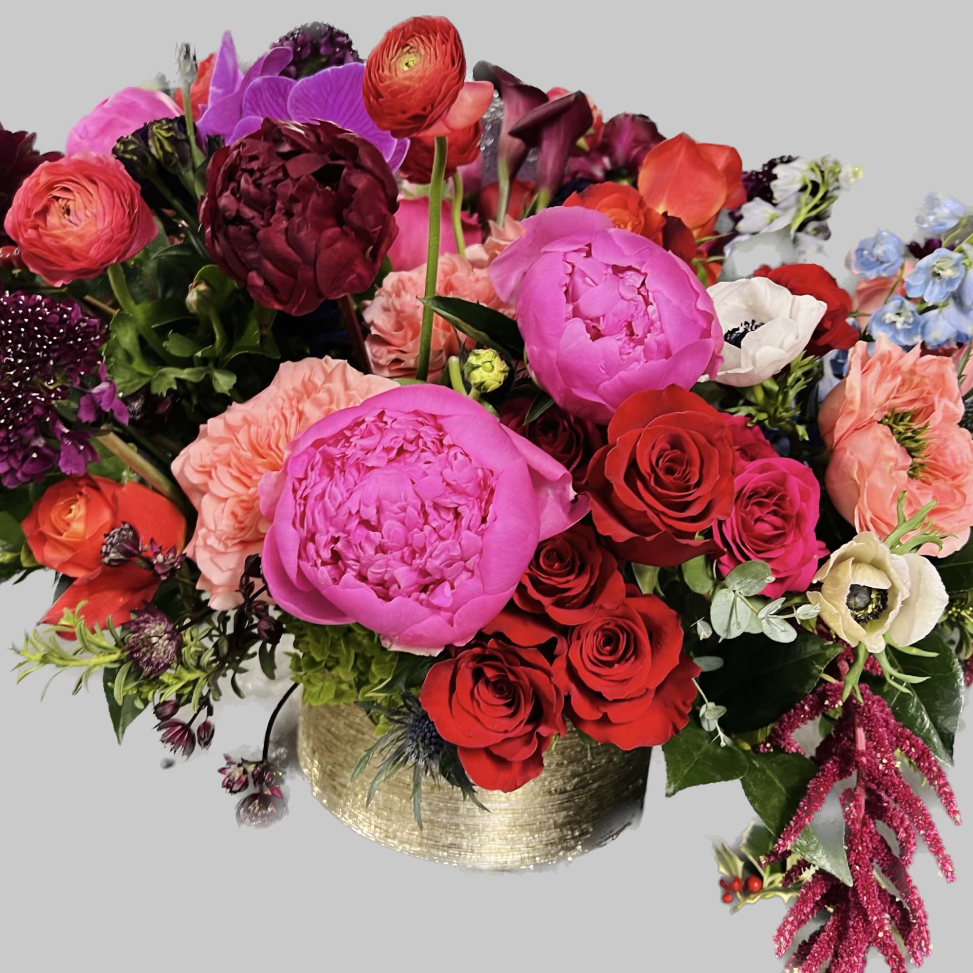 Mixed bouquet of bright pink, red, and purple flowers in a gold vase