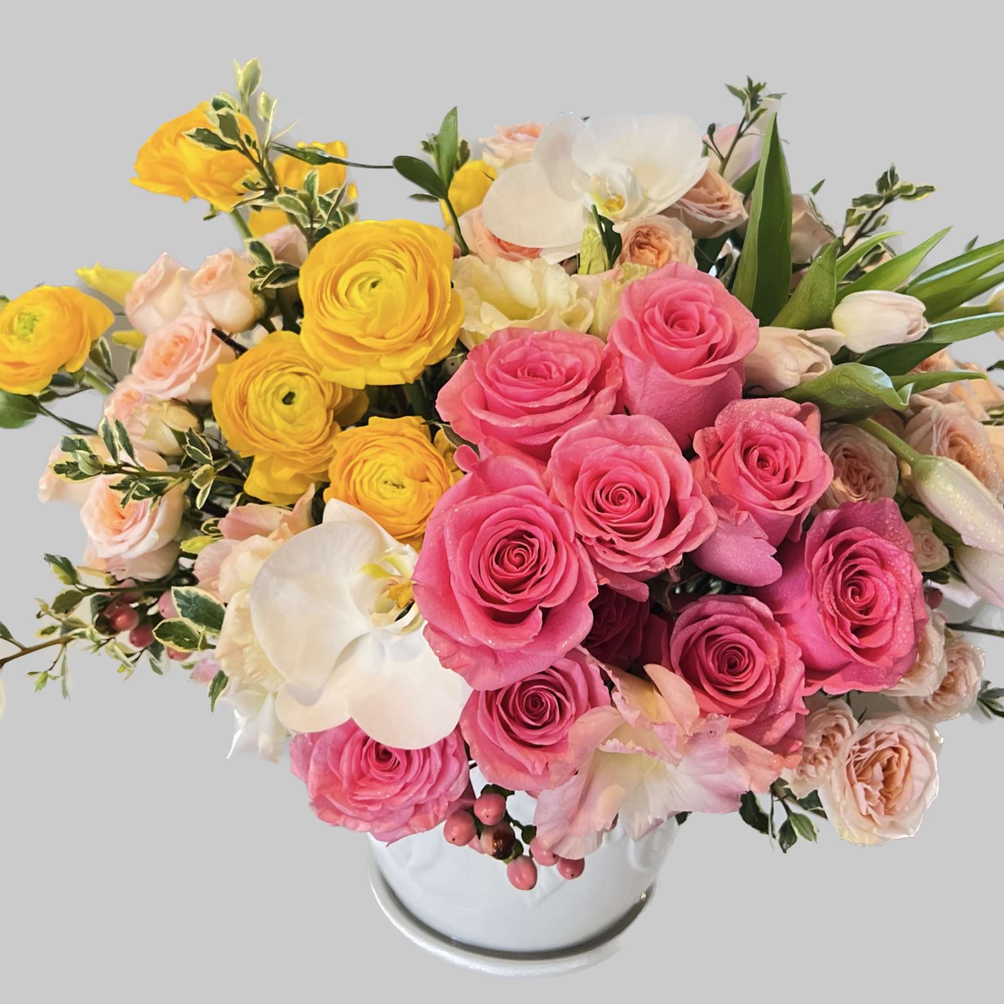 Pink and yellow roses arranged in a white vase with white orchids